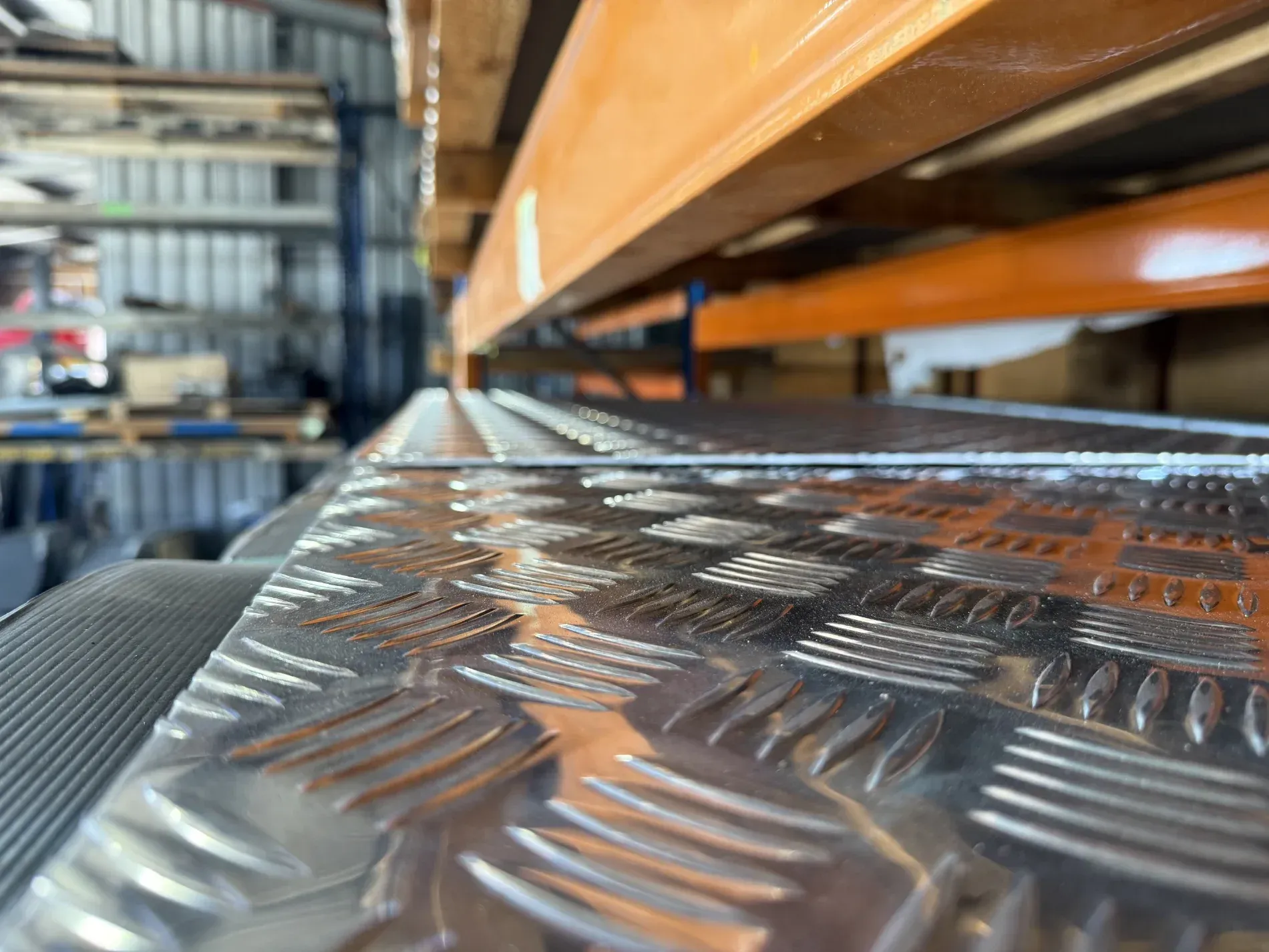 Diamond-plate metal surface with warehouse shelving in the background — Bryants Laser Works in Ipswich, QLD