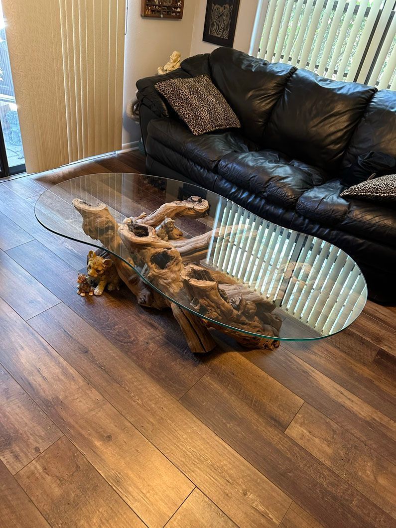 Coffee table with a glass top and driftwood base; black leather sofa in background.