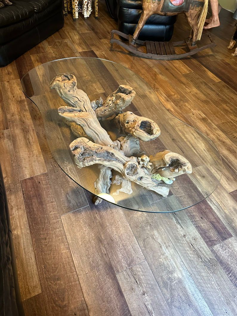 Oval glass coffee table with driftwood base on a wood floor.
