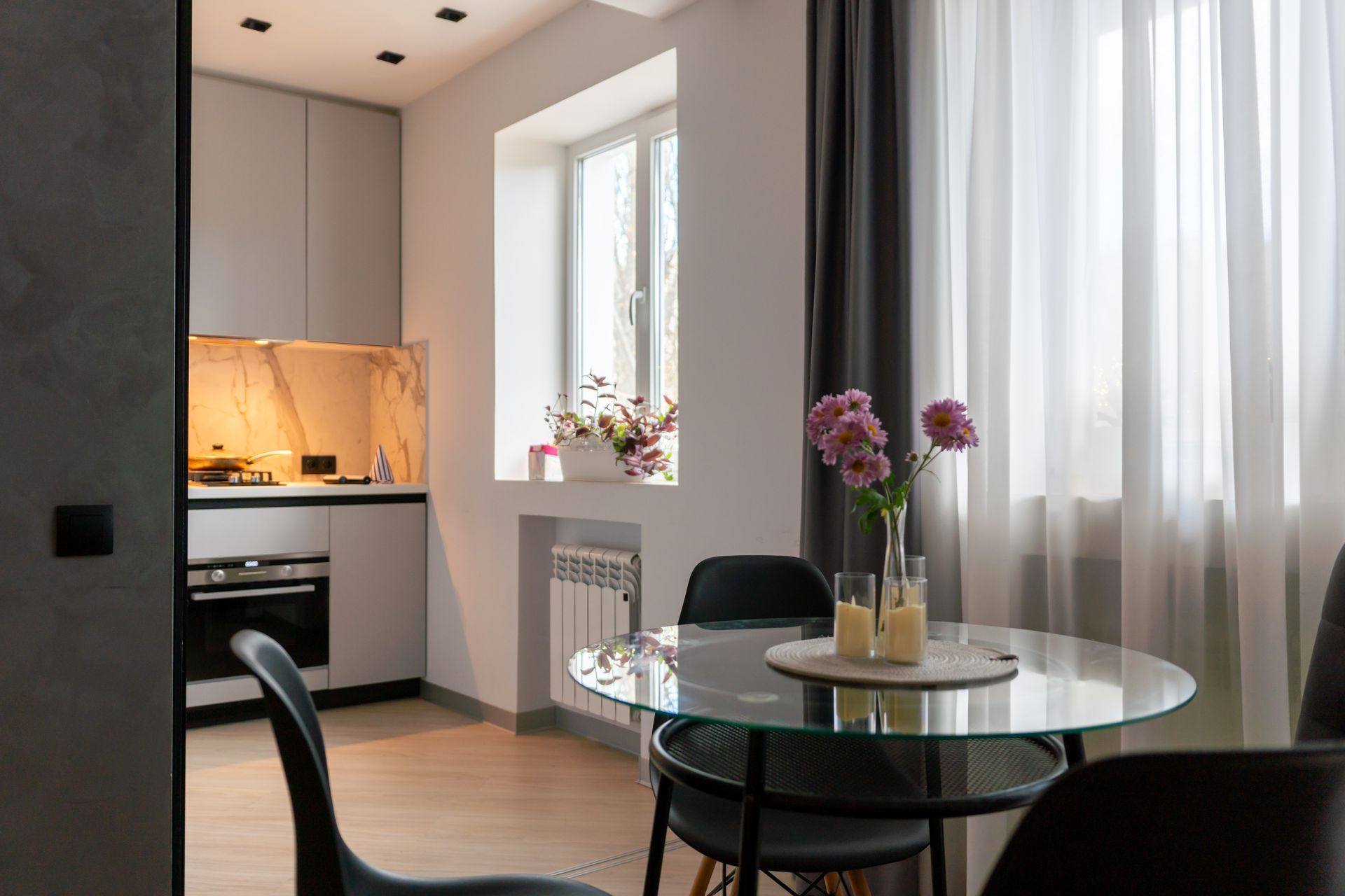 Modern kitchen and dining area with a round glass table and flowers.