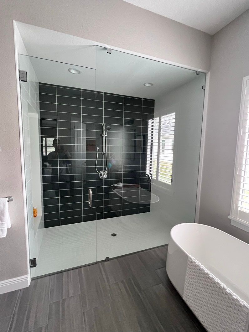 Modern bathroom with glass shower enclosure, black tile accent wall, white tub.