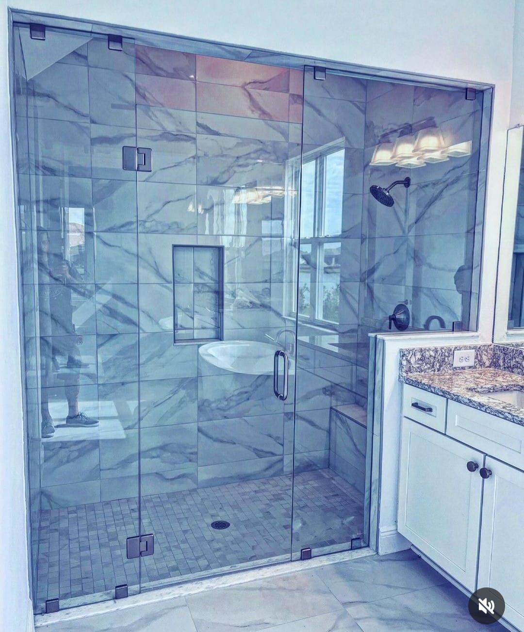 Glass-enclosed shower with marble tile walls and a built-in bench. Bathroom with a white vanity.