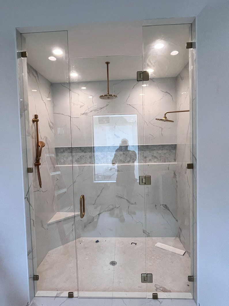 Glass-enclosed shower with gold fixtures; white marble walls, two shower heads, and a built-in seat.