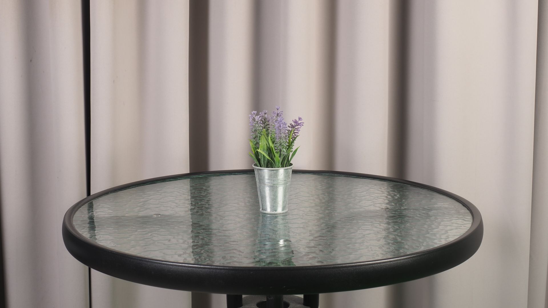 Small potted plant on a glass table in front of a neutral-colored curtain.