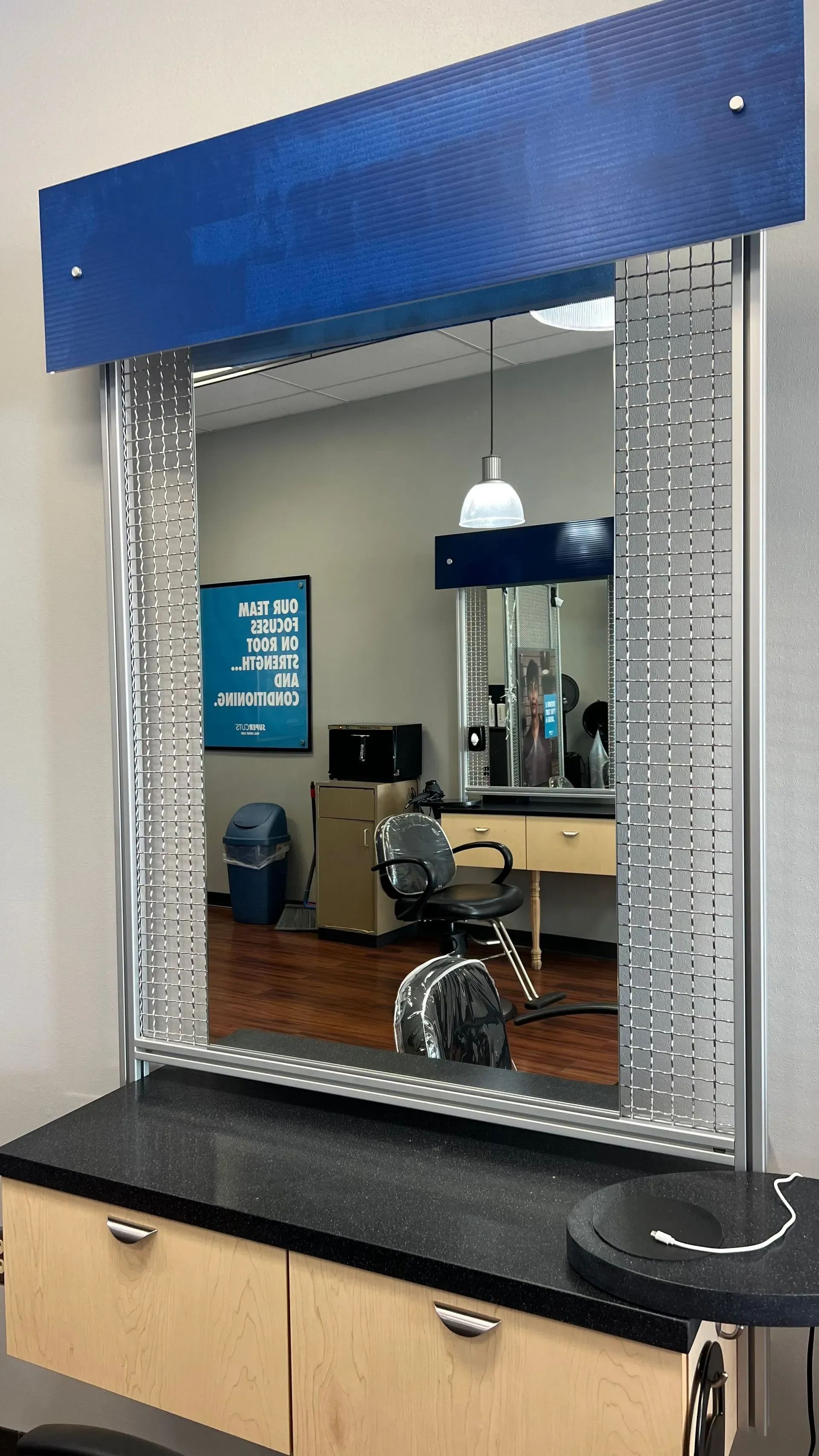 Mirror in a salon, framed with silver detail. Dark counter, blue top accent, and shop interior visible.