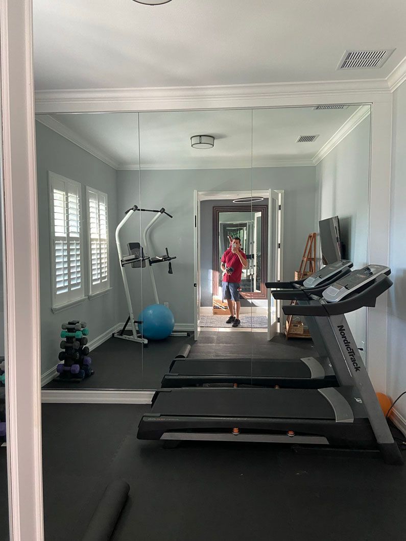 Gym interior with treadmills, weight rack, and a person reflected in a large mirror.