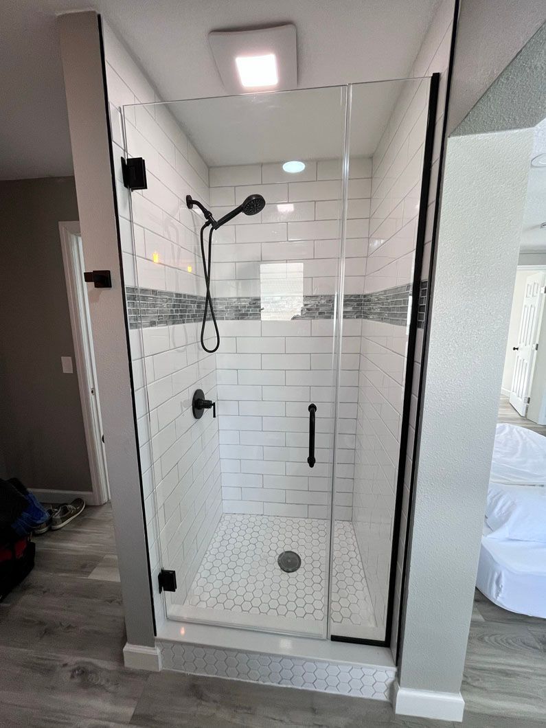 Modern glass shower with white and gray tile, black hardware, and pebble flooring.