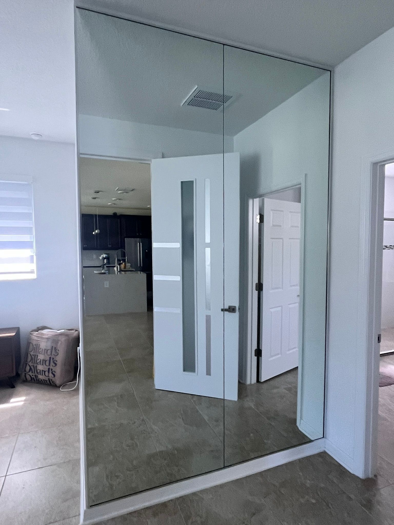 Large mirror on wall reflects interior with doors, kitchen, and light-colored flooring.