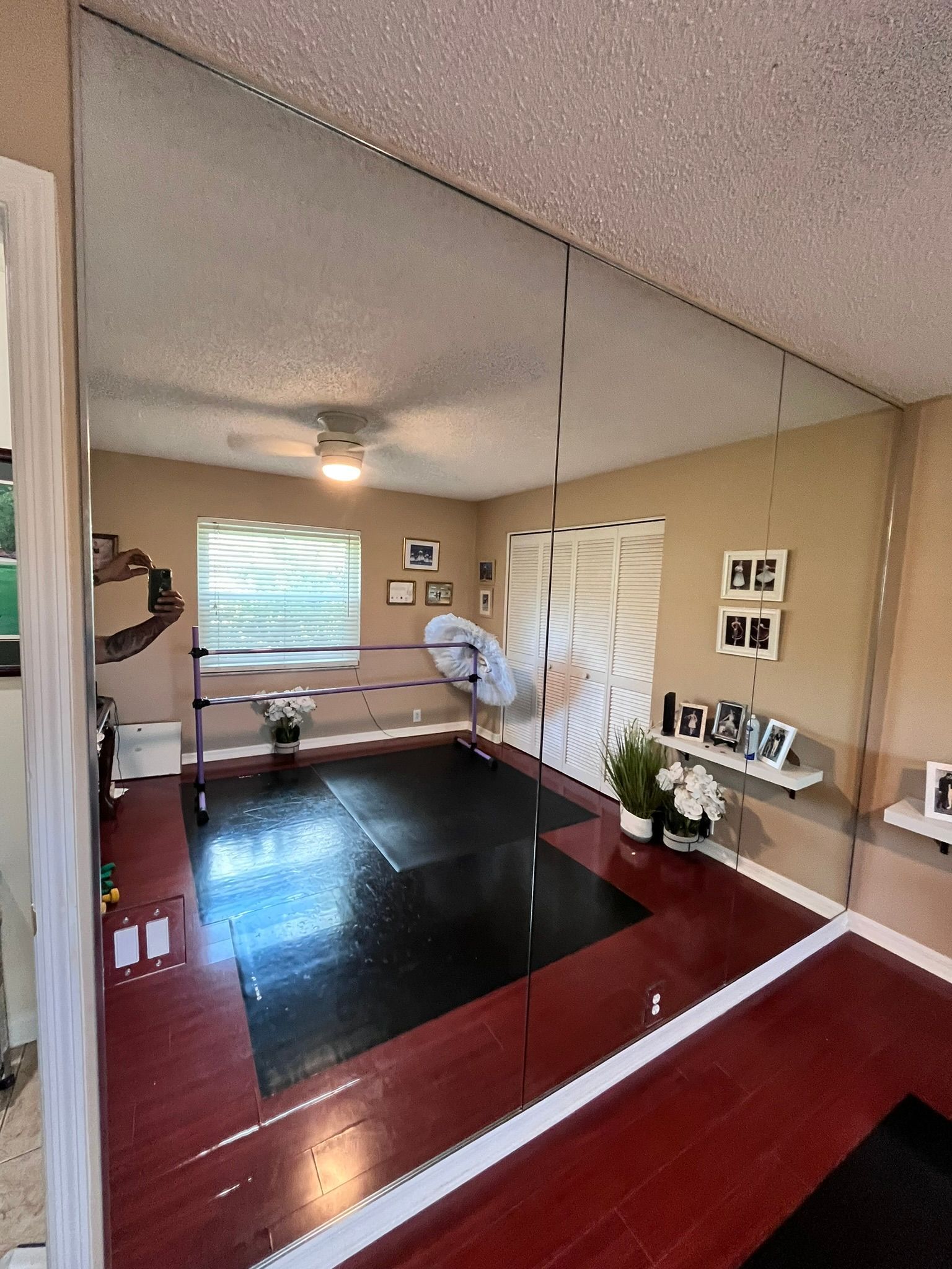 Dance studio with mirrors, barre, black mat, and red floor. Sunlight streams through a window.