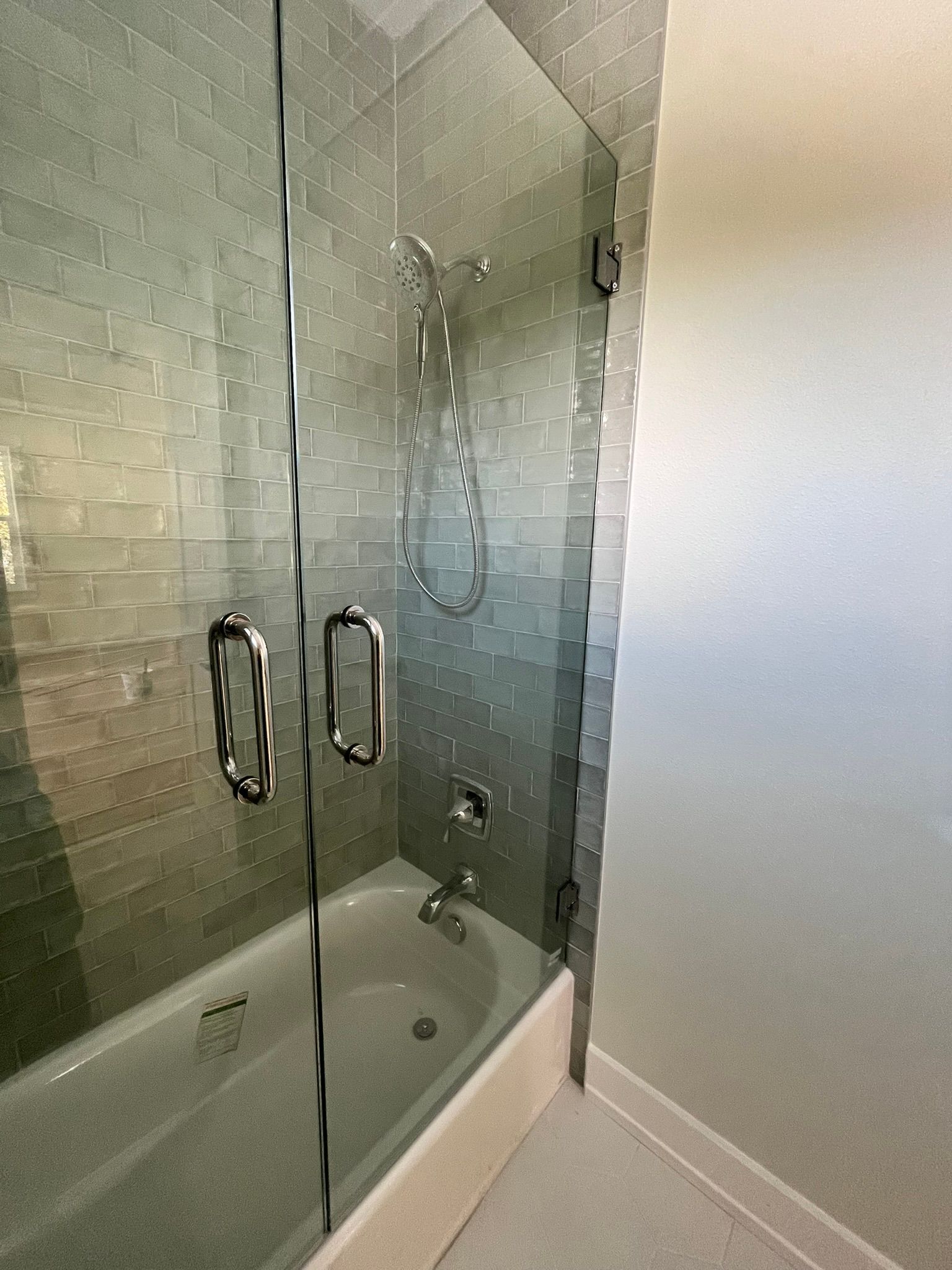 Shower with glass doors and chrome fixtures, adjacent to a tiled wall and white tub.