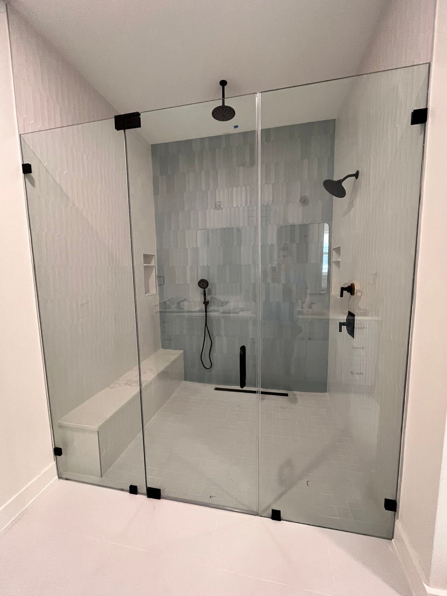 Modern shower with glass walls, black hardware, a built-in bench, and light blue tiled wall.