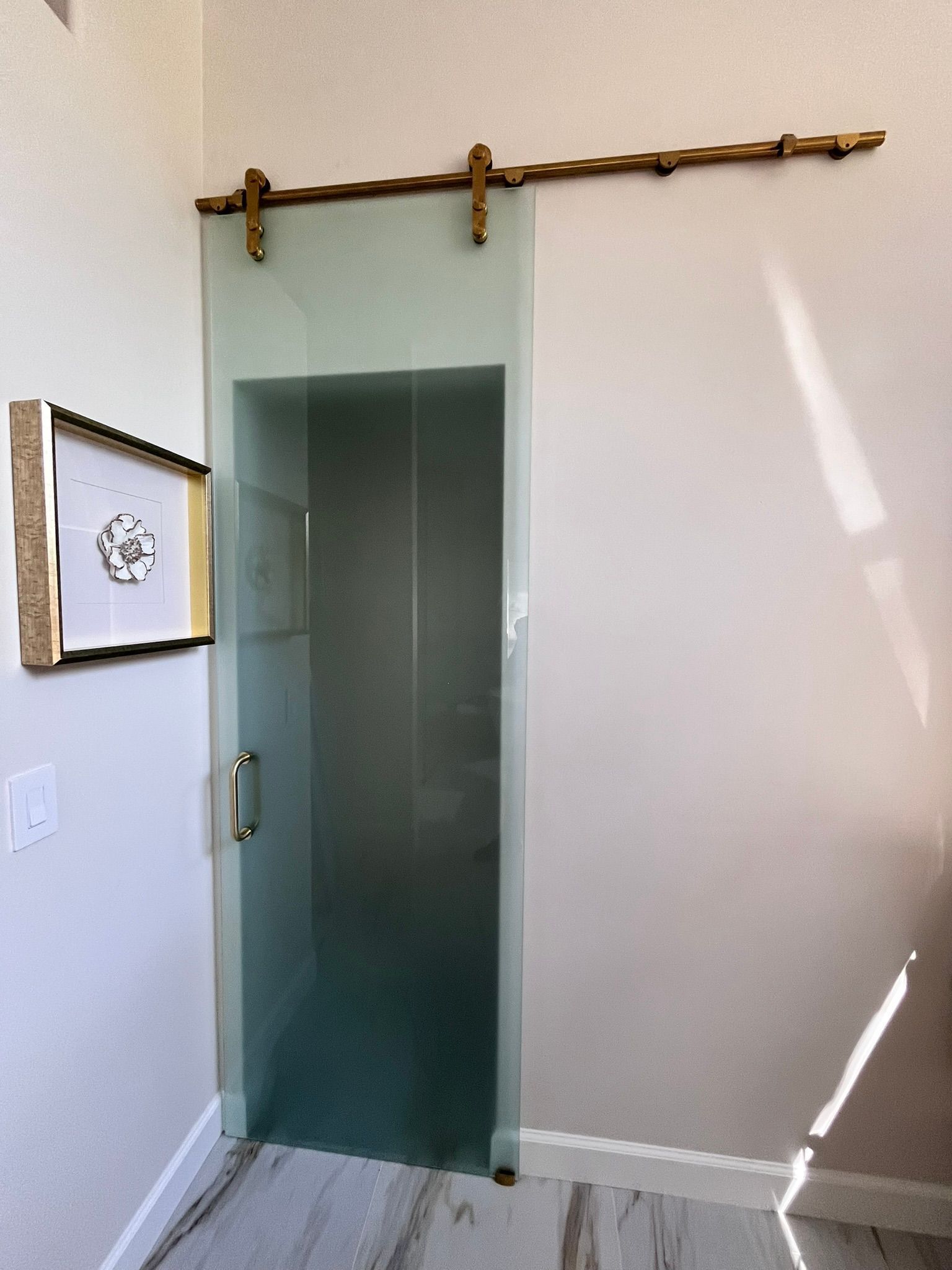 Frosted glass sliding door, brass hardware, framed artwork on wall, hardwood floor.