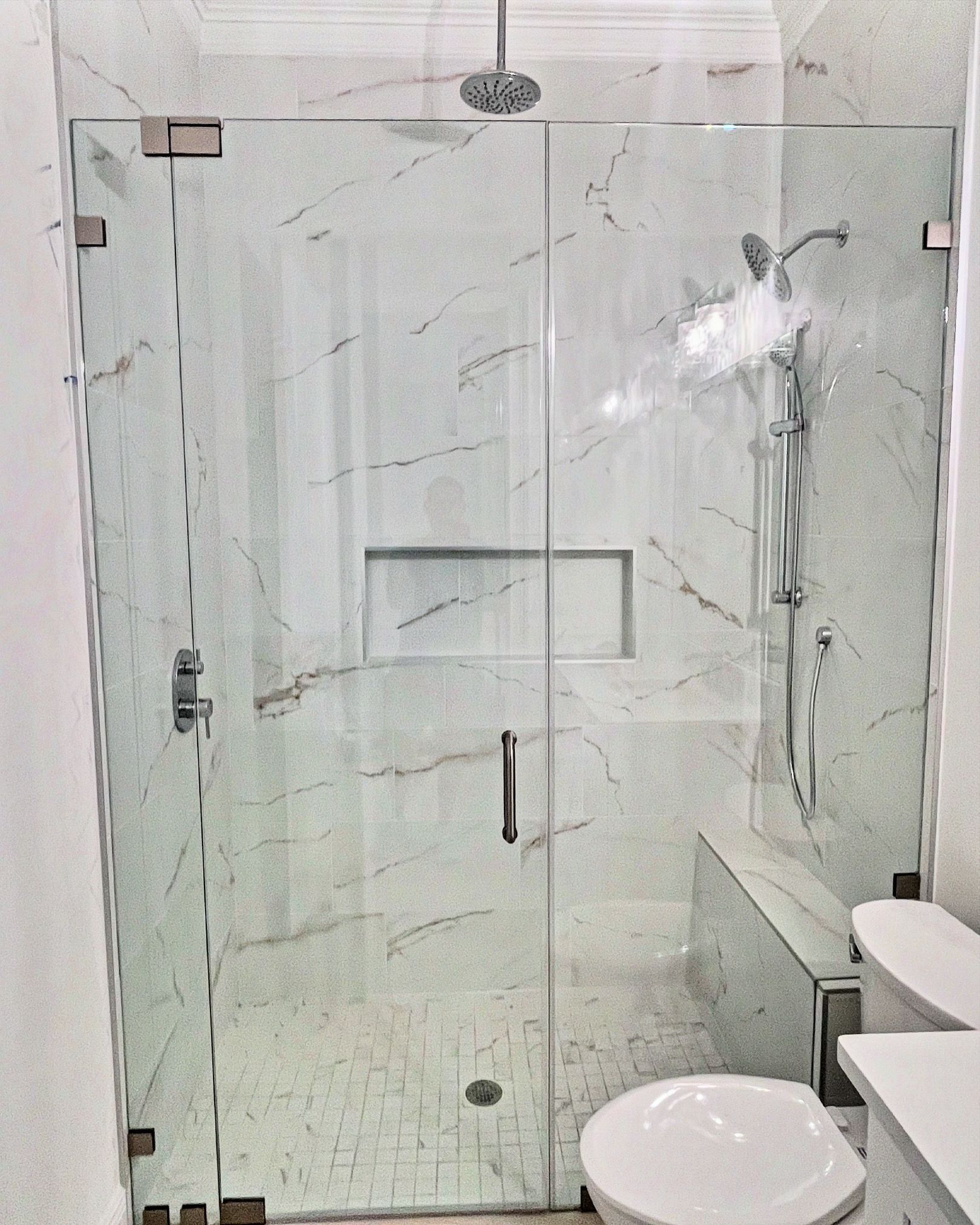 Glass shower enclosure with marble tile walls, a toilet, and shower fixtures.