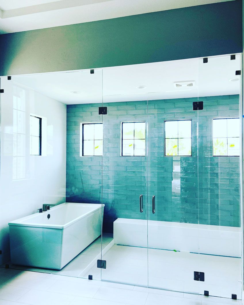 Modern bathroom with a white tub, teal tiled wall, and glass shower enclosure.