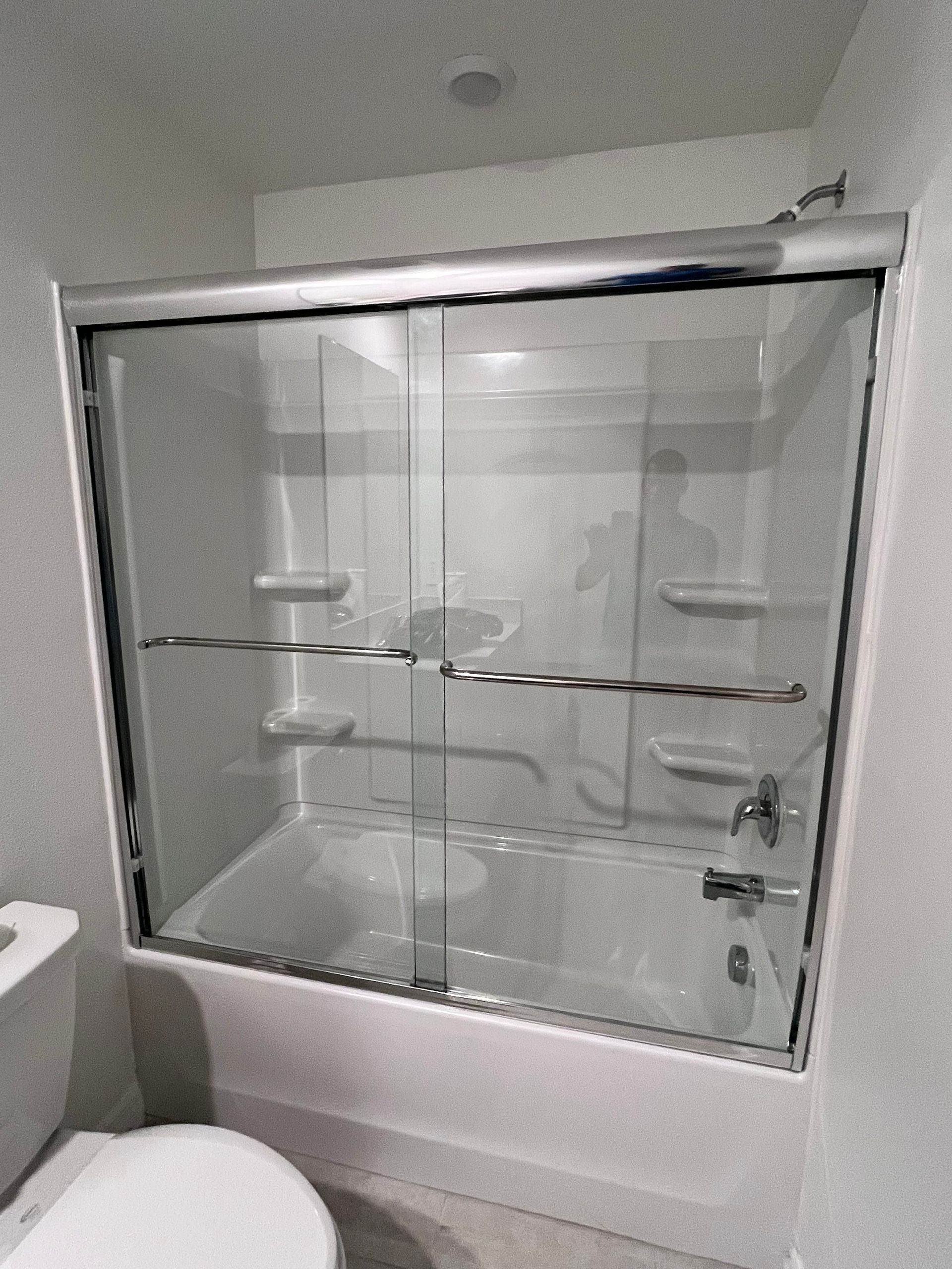 A white bathroom with a glass sliding door shower enclosure over a bathtub. A toilet is visible to the left.