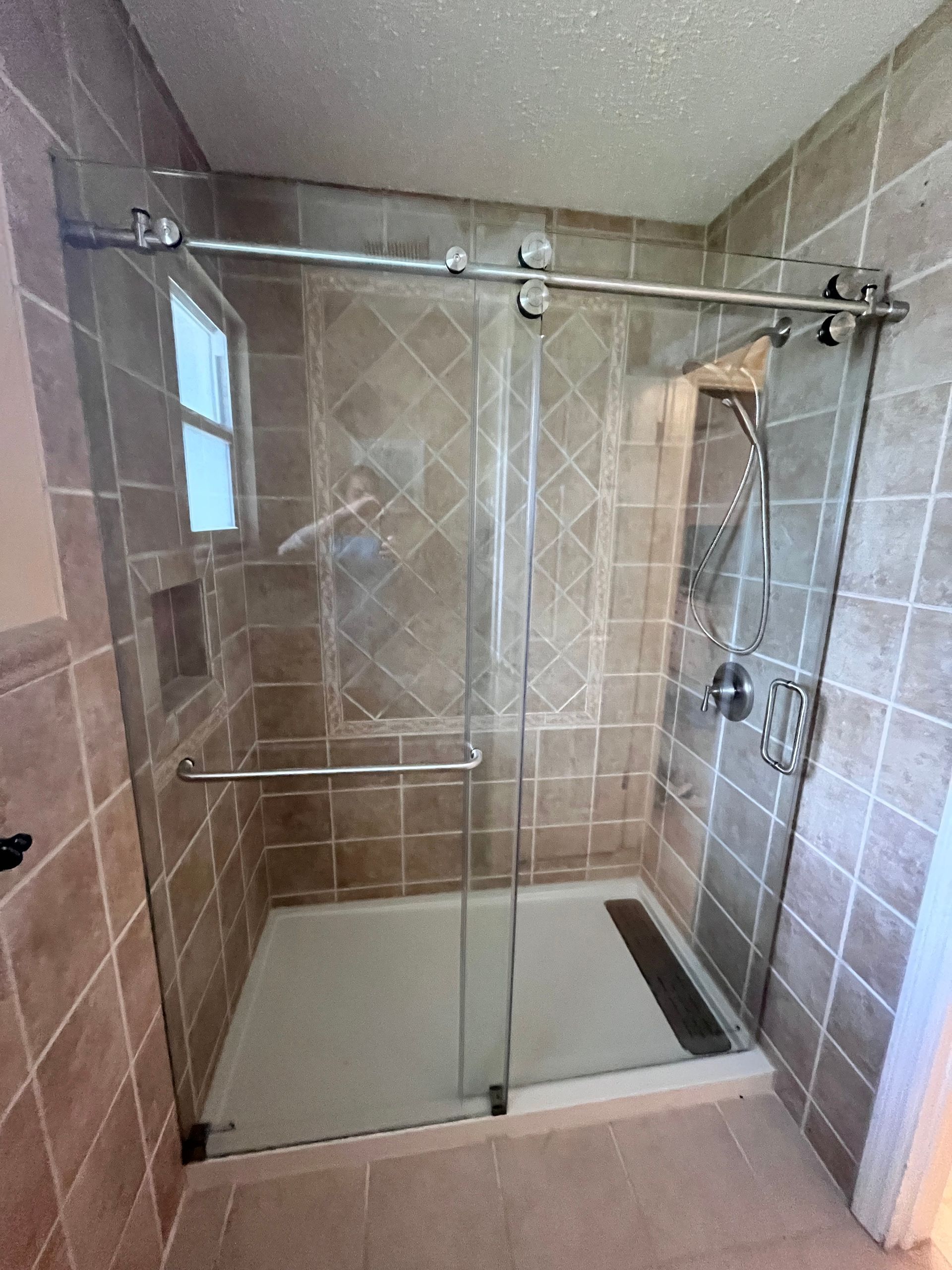 Modern shower stall with sliding glass doors, brown tiled walls, and stainless steel hardware.