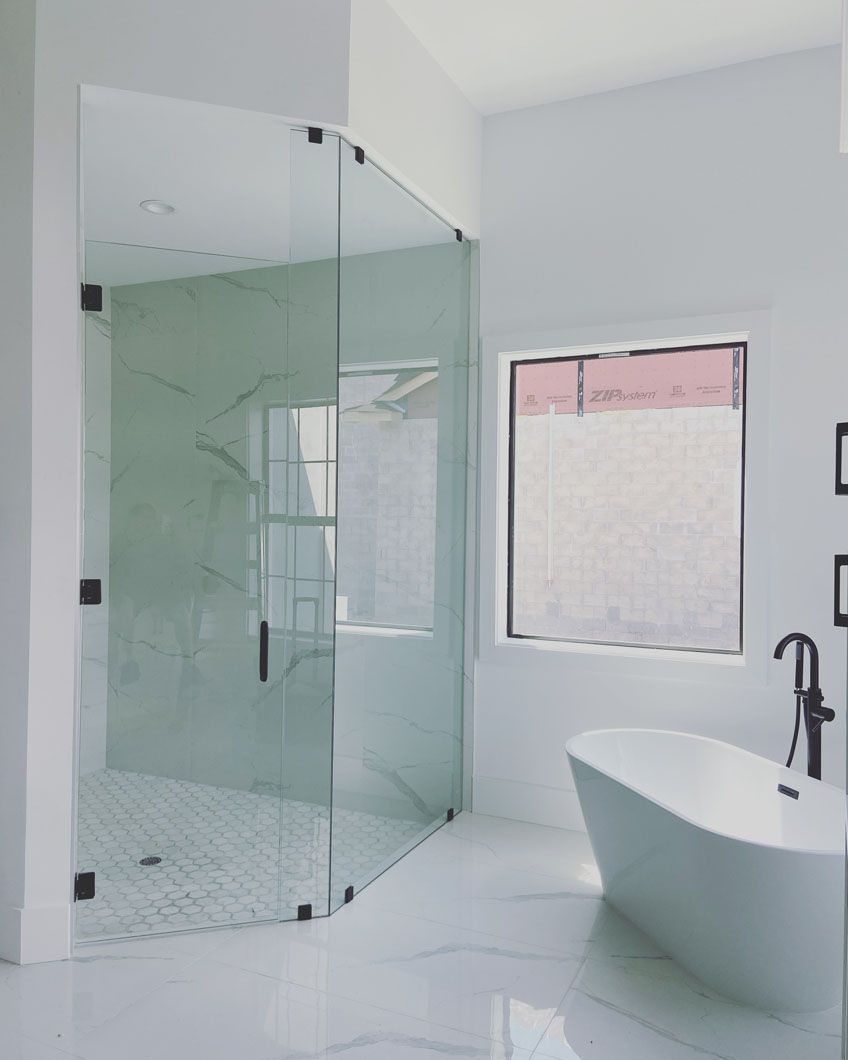 Modern white bathroom with glass shower, freestanding tub, and window.
