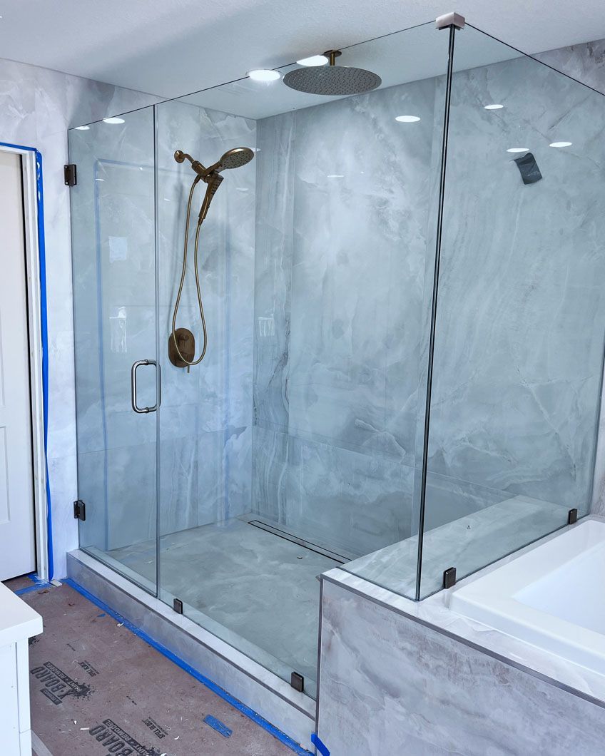 Glass shower enclosure with gray marble-like walls and bronze shower fixtures.