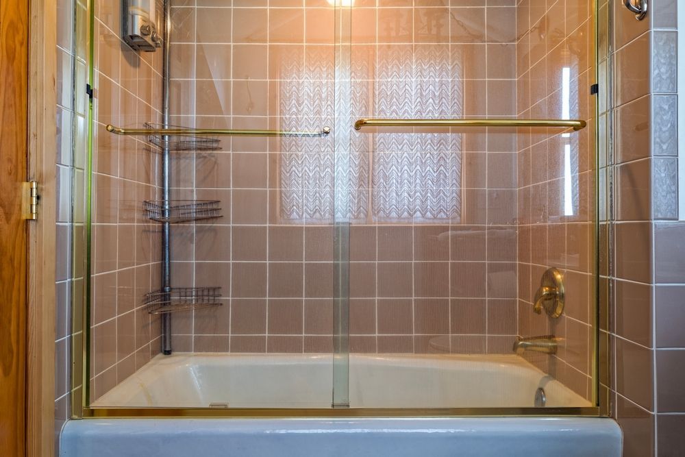 Glass shower enclosure with black hardware, white bench, and blue-tiled wall.