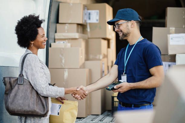 Woman and delivery man shaking hands near a van full of boxes. Both are smiling.