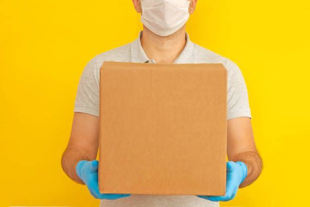 Delivery person carrying a cardboard box next to a van, looking away.