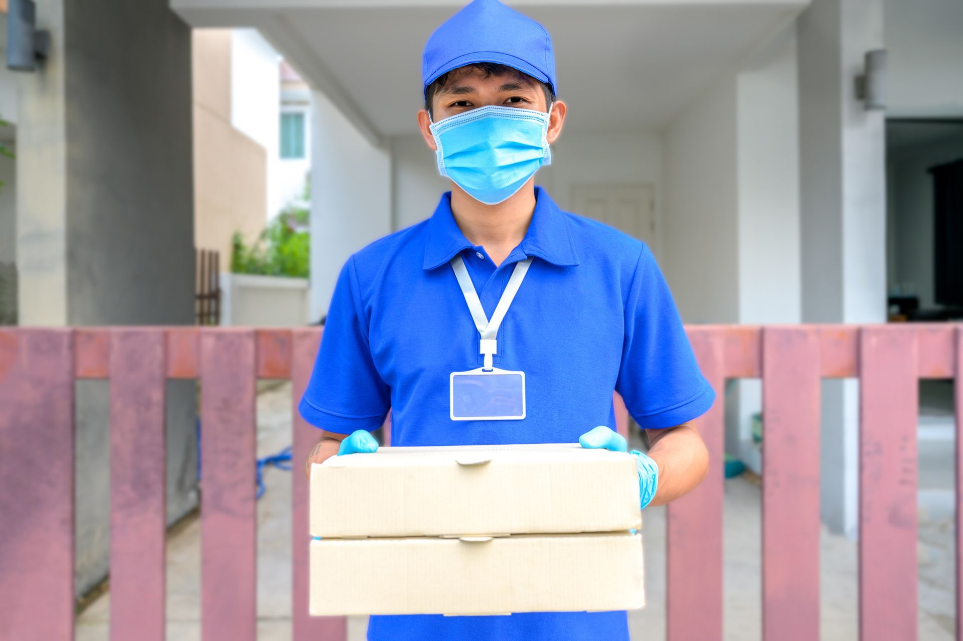 Delivery person in blue uniform, mask, gloves, holding two pizza boxes.