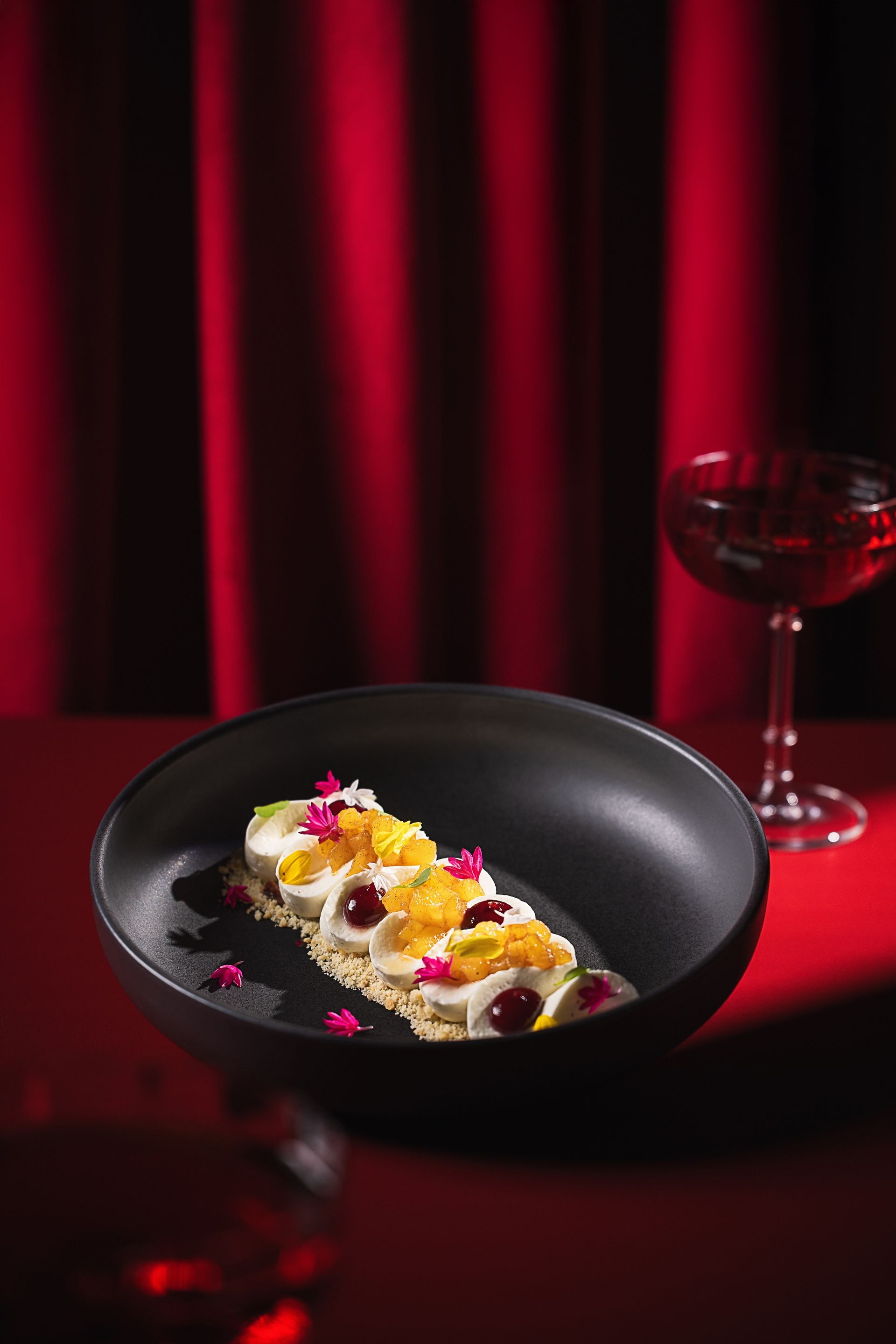 A black bowl filled with food and a glass of wine on a table.