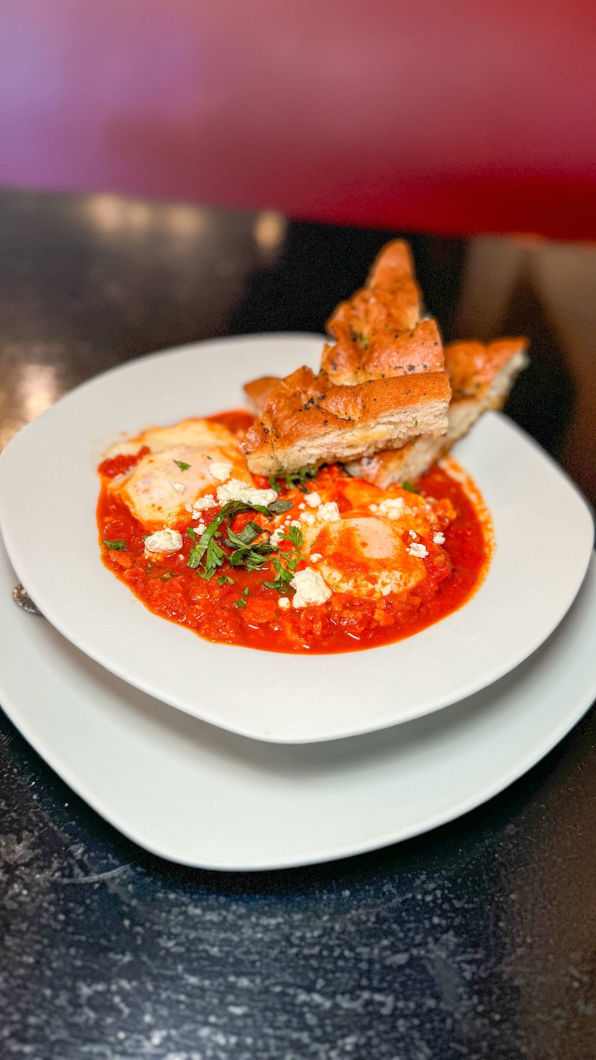 A white plate topped with a bowl of soup and bread on a table.