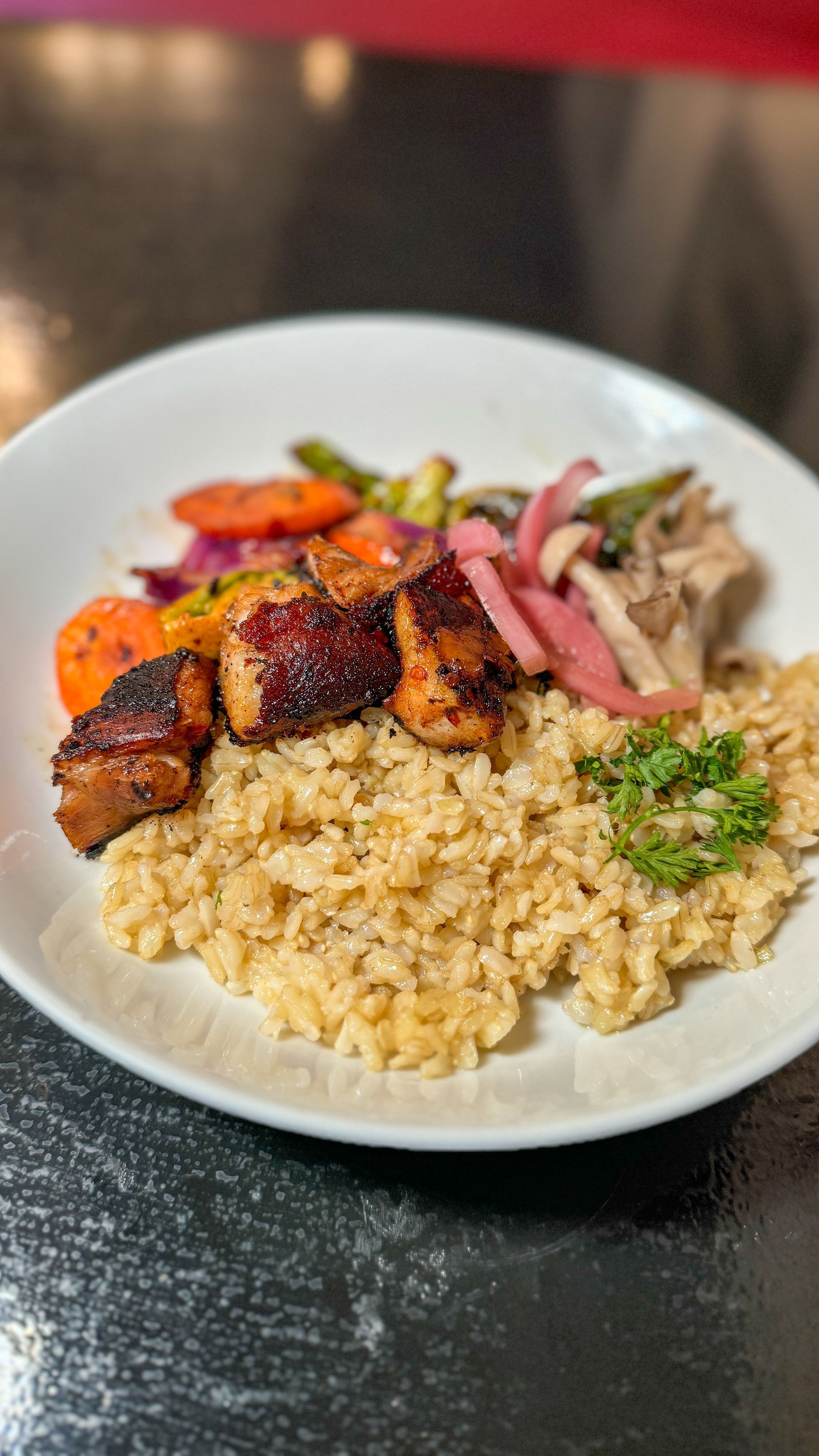 A white plate topped with rice , meat and vegetables on a table.