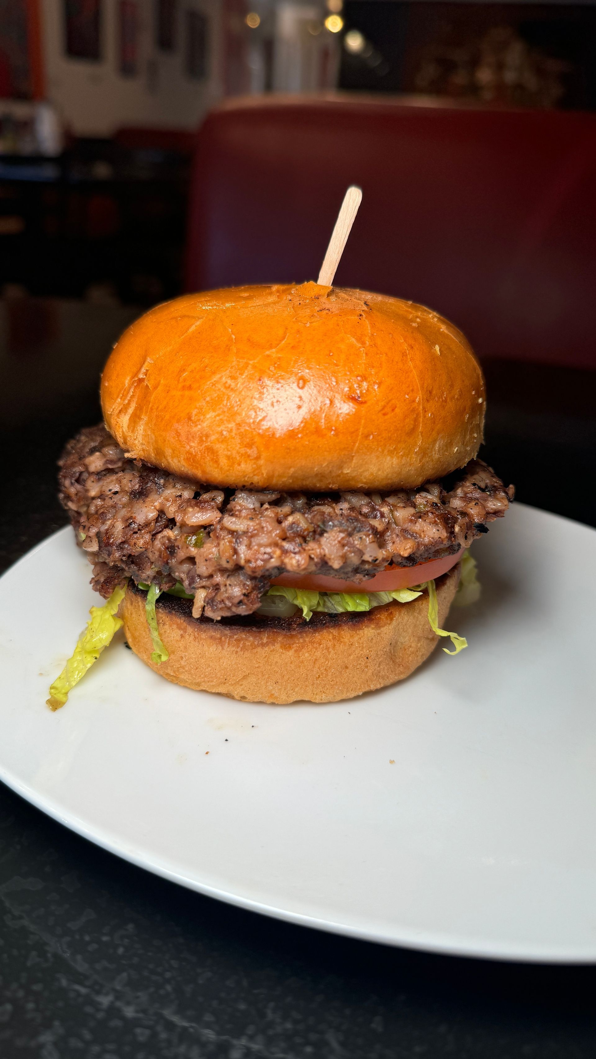 A hamburger on a white plate with a toothpick in it.