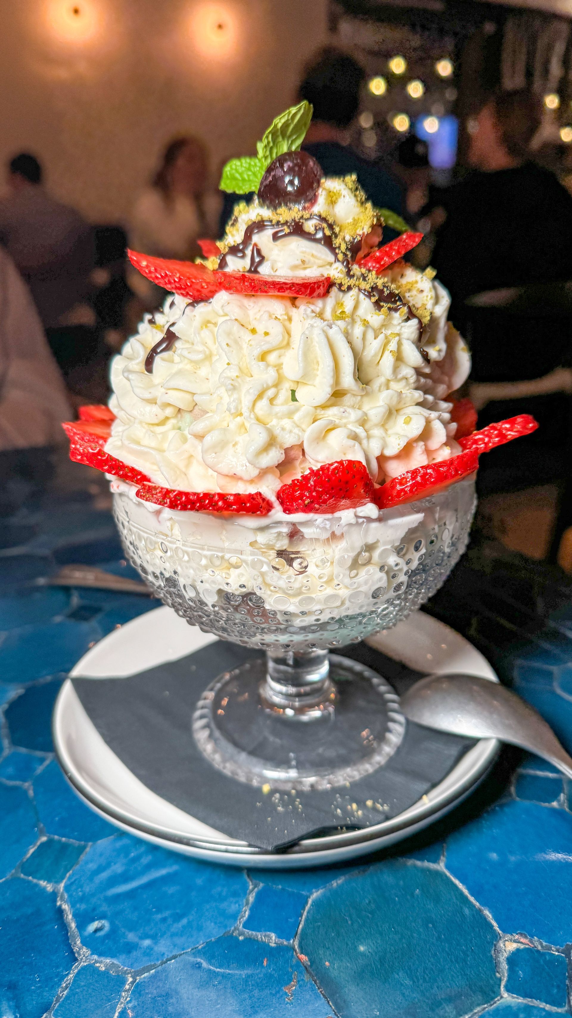 A dessert with whipped cream and strawberries in a glass bowl on a plate.