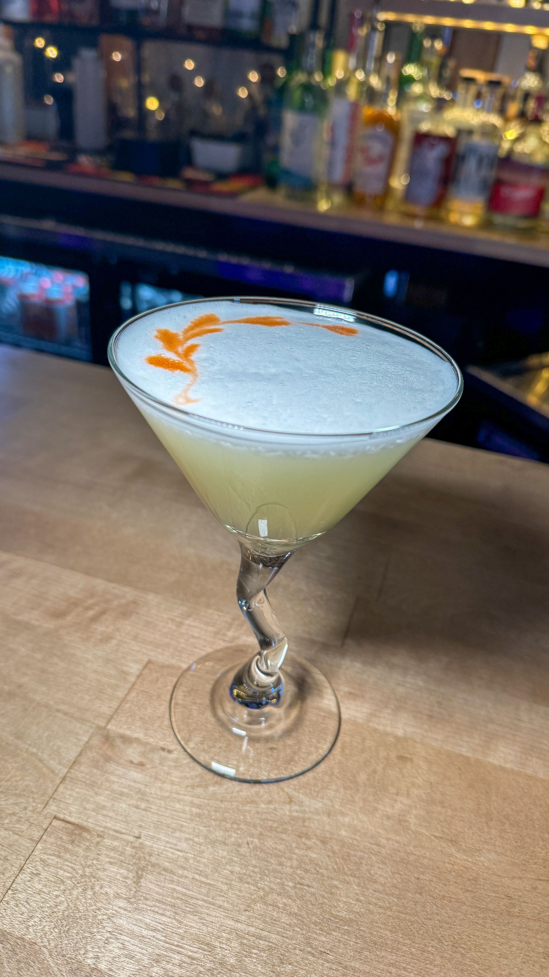 A martini glass filled with a yellow liquid is sitting on a wooden table.