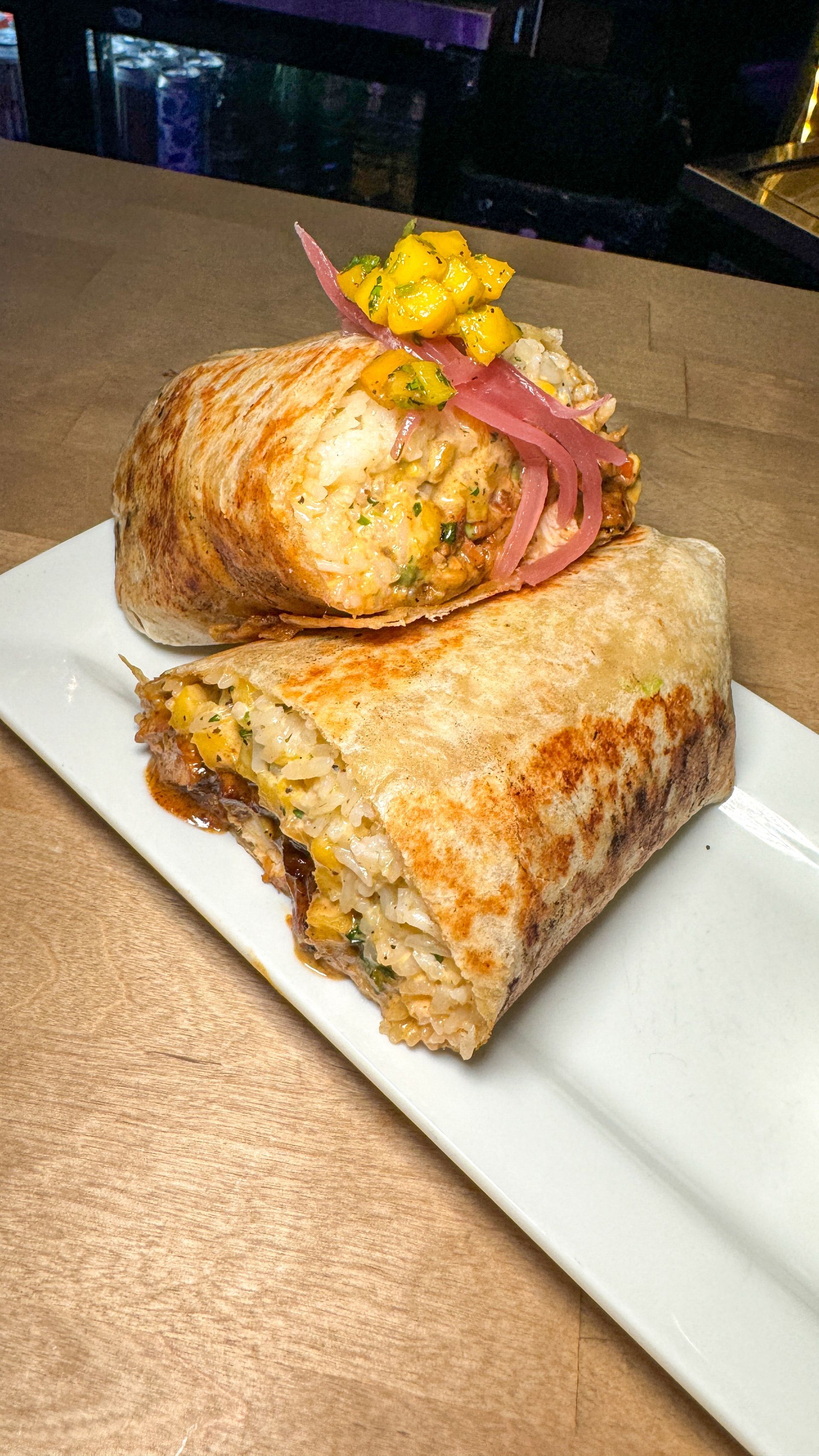 A burrito is sitting on a white plate on a table.