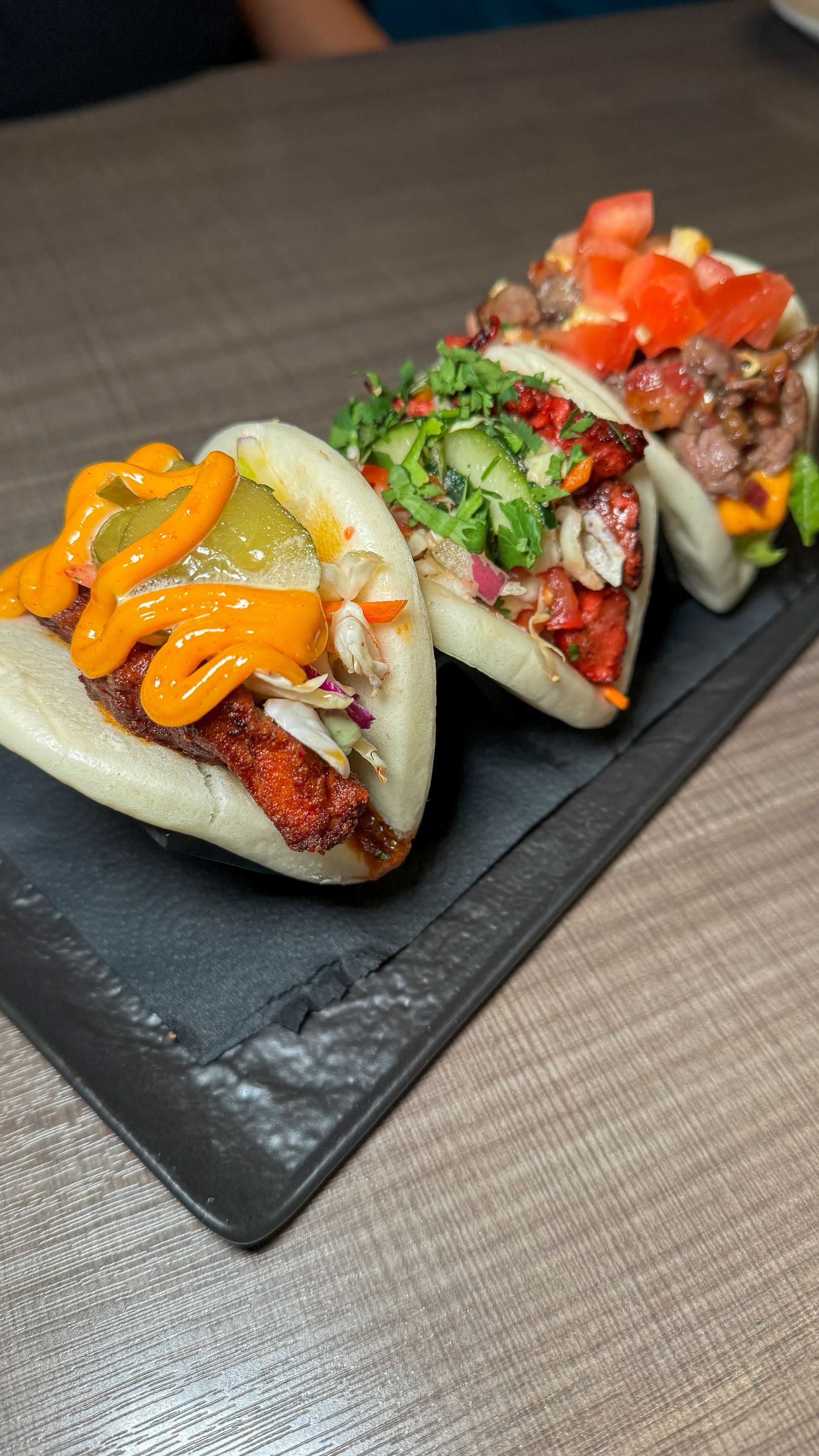 A close up of three sandwiches on a black plate on a table.