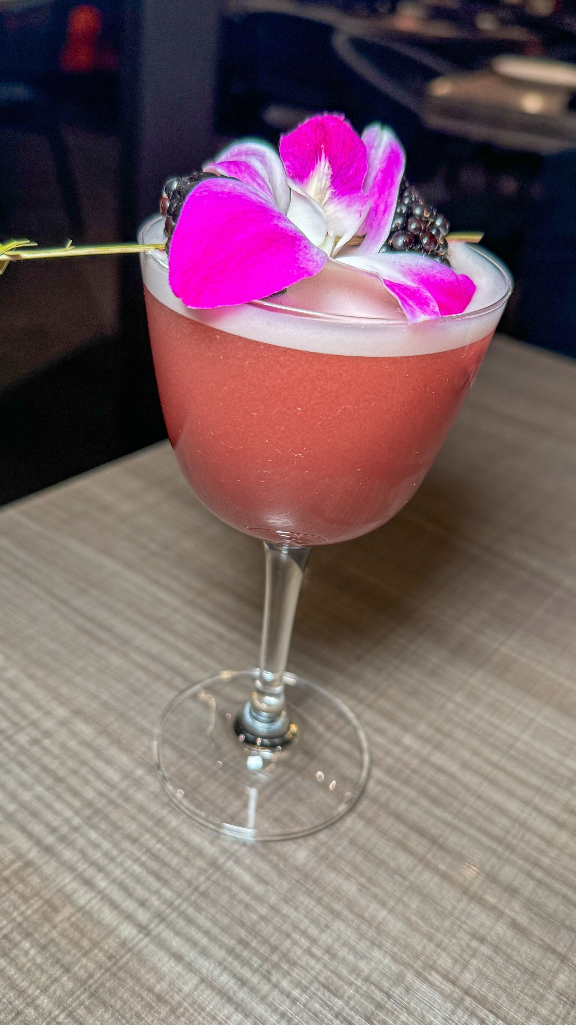 A close up of a pink cocktail in a martini glass on a table.