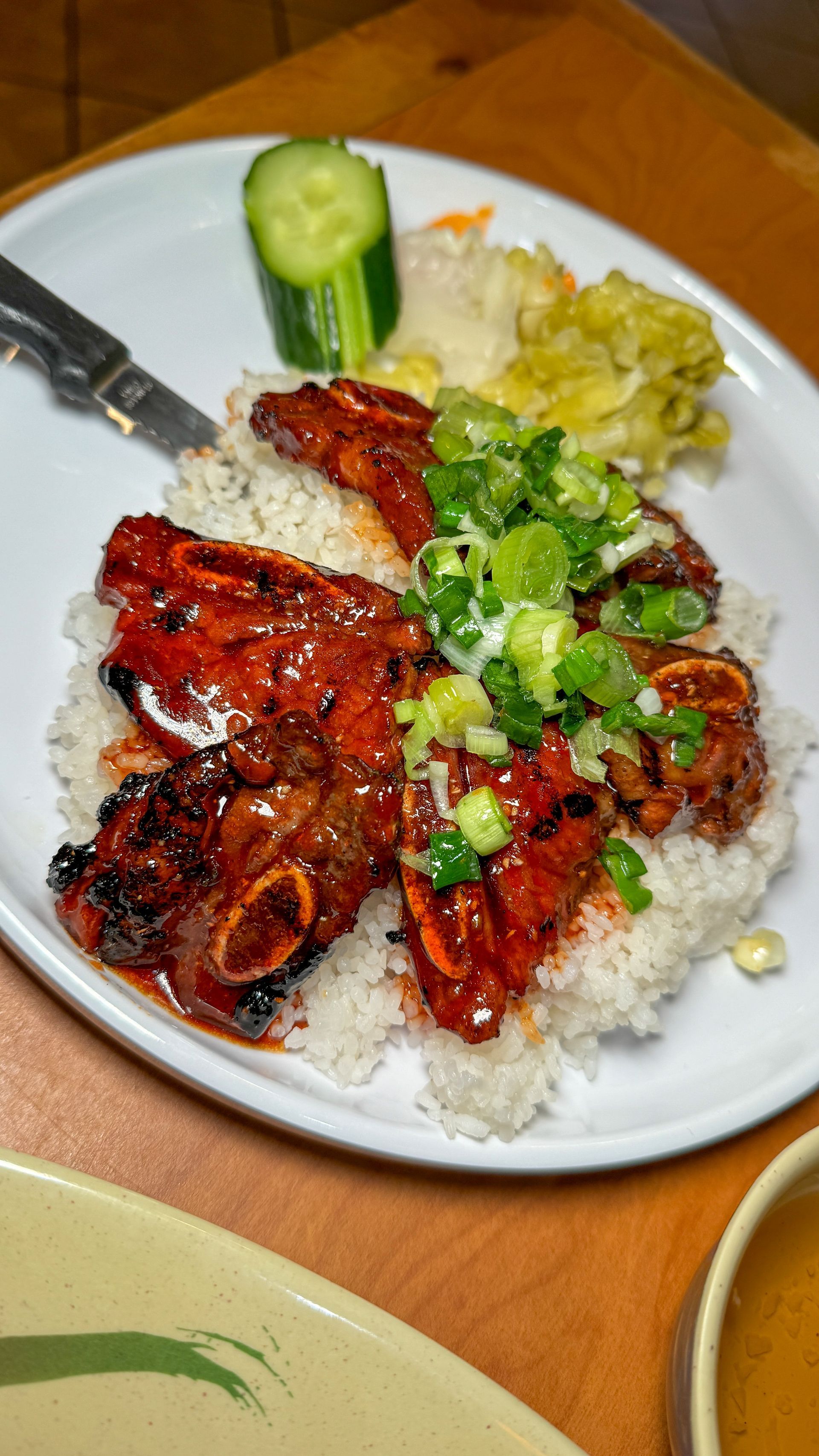 A plate of food with rice , meat and vegetables on a wooden table.