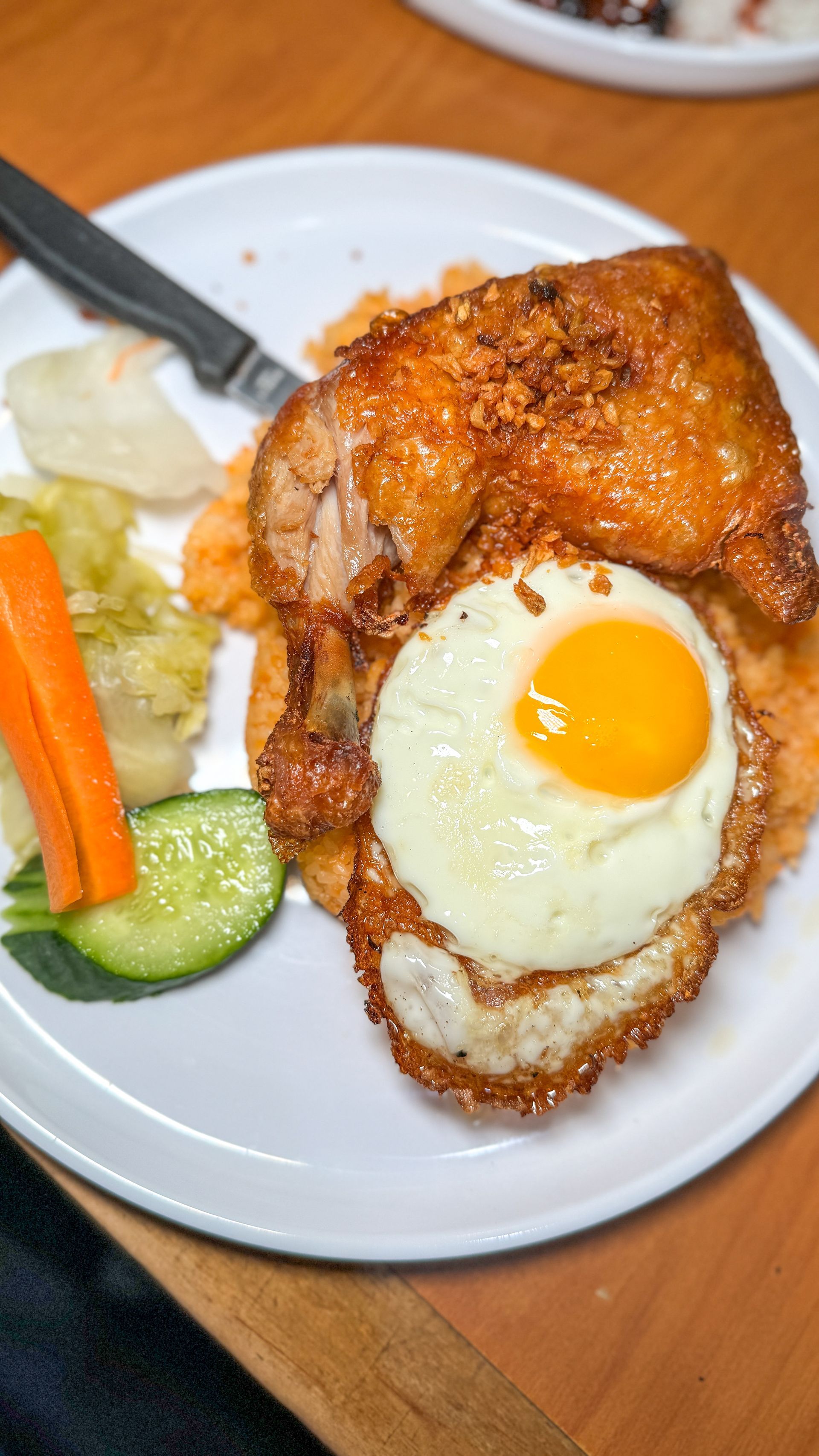 A plate of food with fried chicken , eggs , carrots and cucumbers on a table.