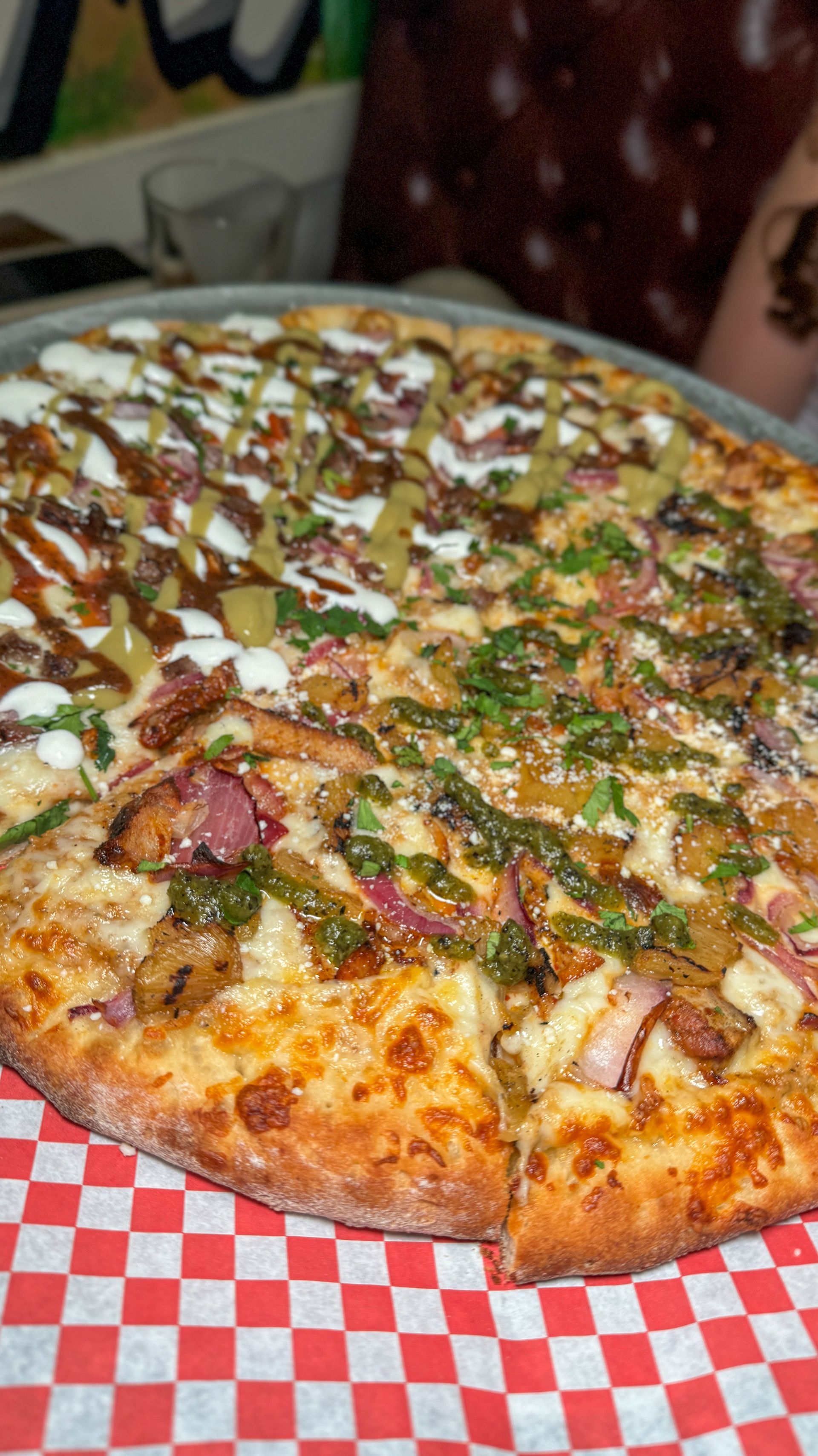 A pizza is sitting on a checkered paper on a table.