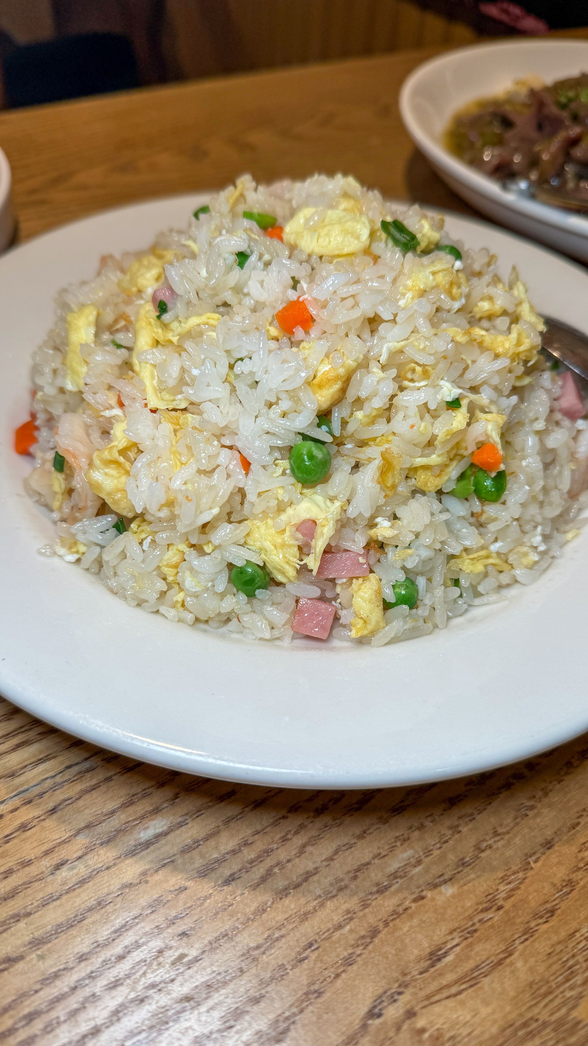 A white plate topped with rice and vegetables on a wooden table.