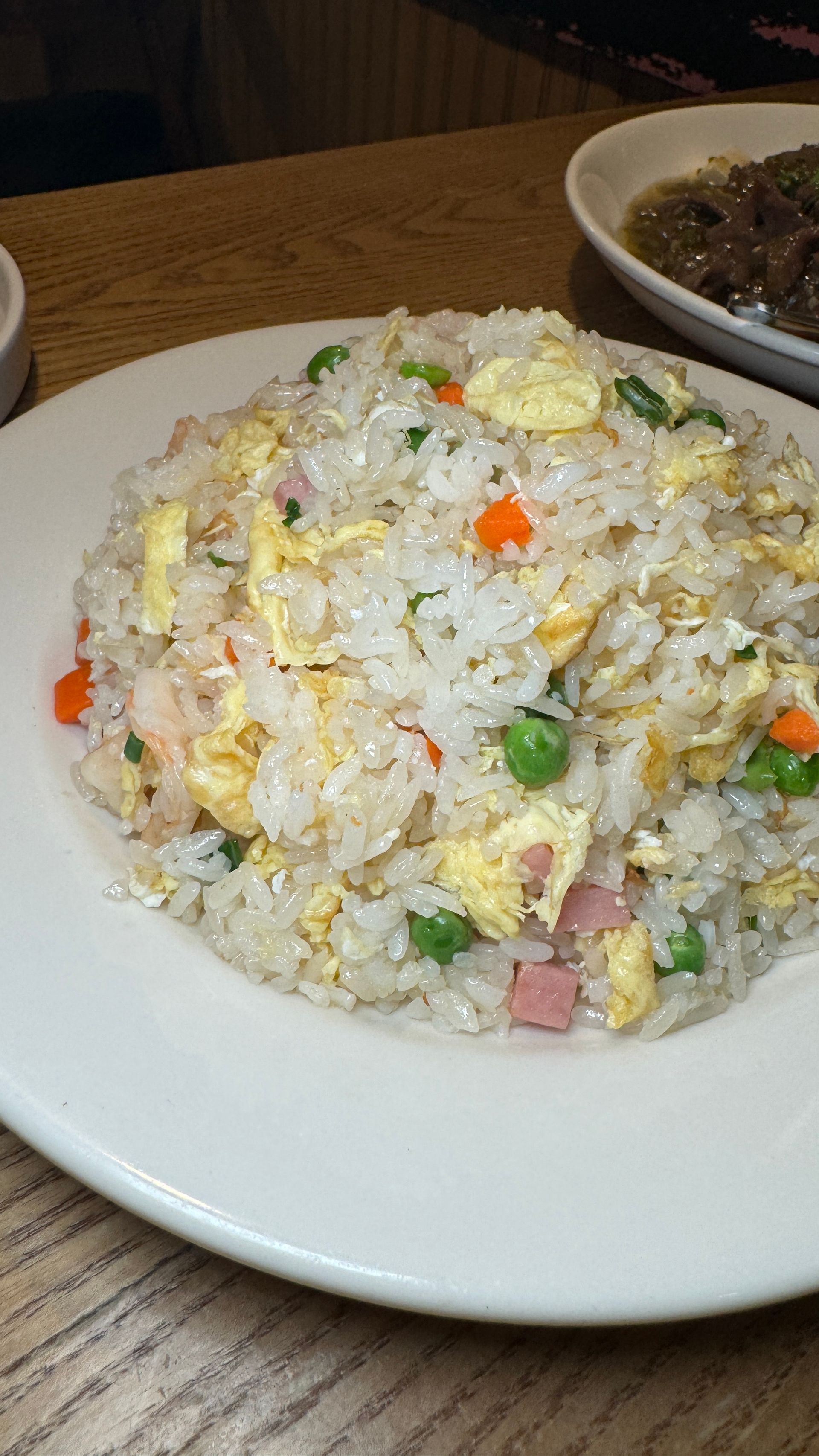 A white plate topped with rice and vegetables on a wooden table.