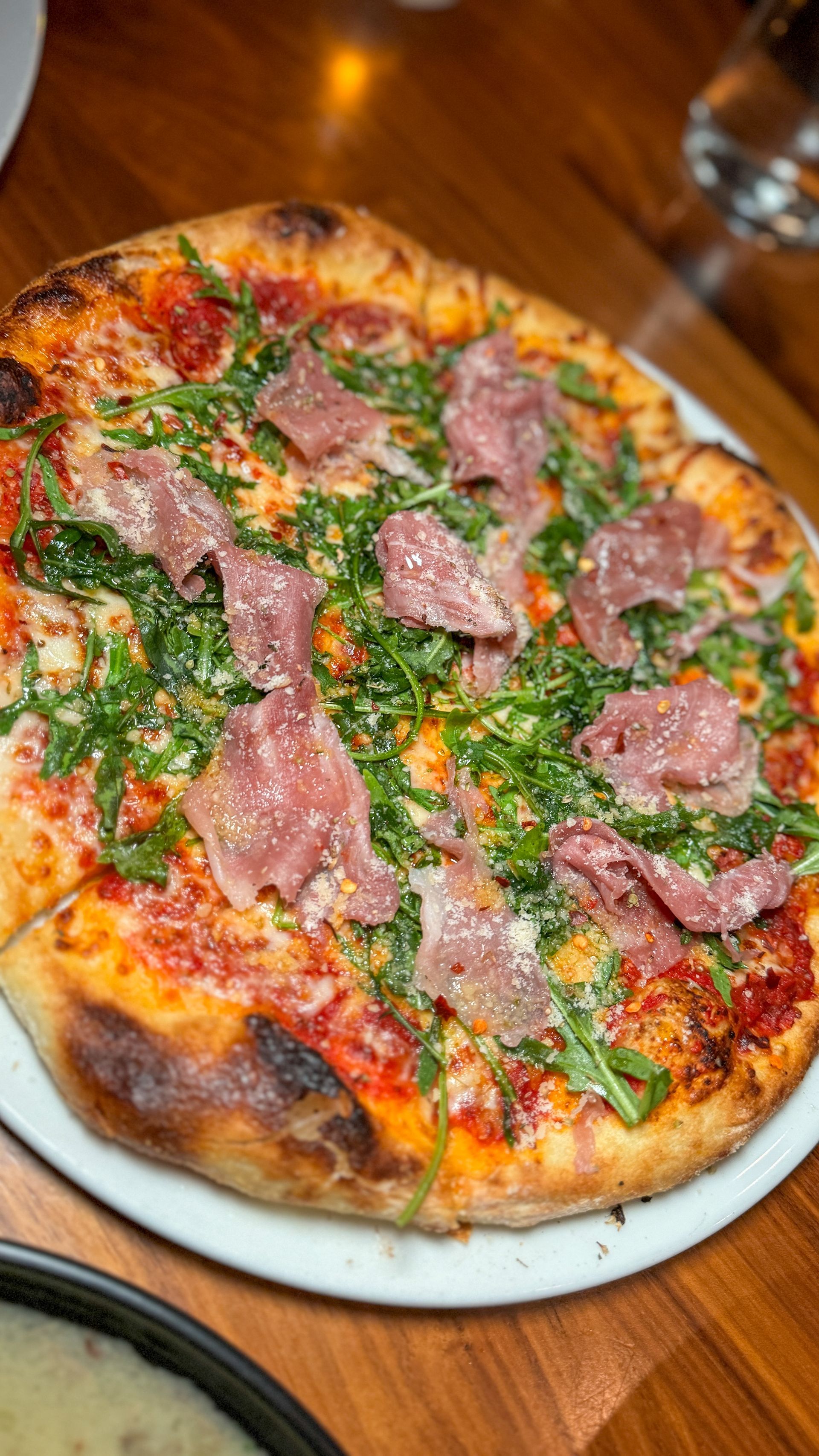 A pizza is sitting on a white plate on a wooden table.