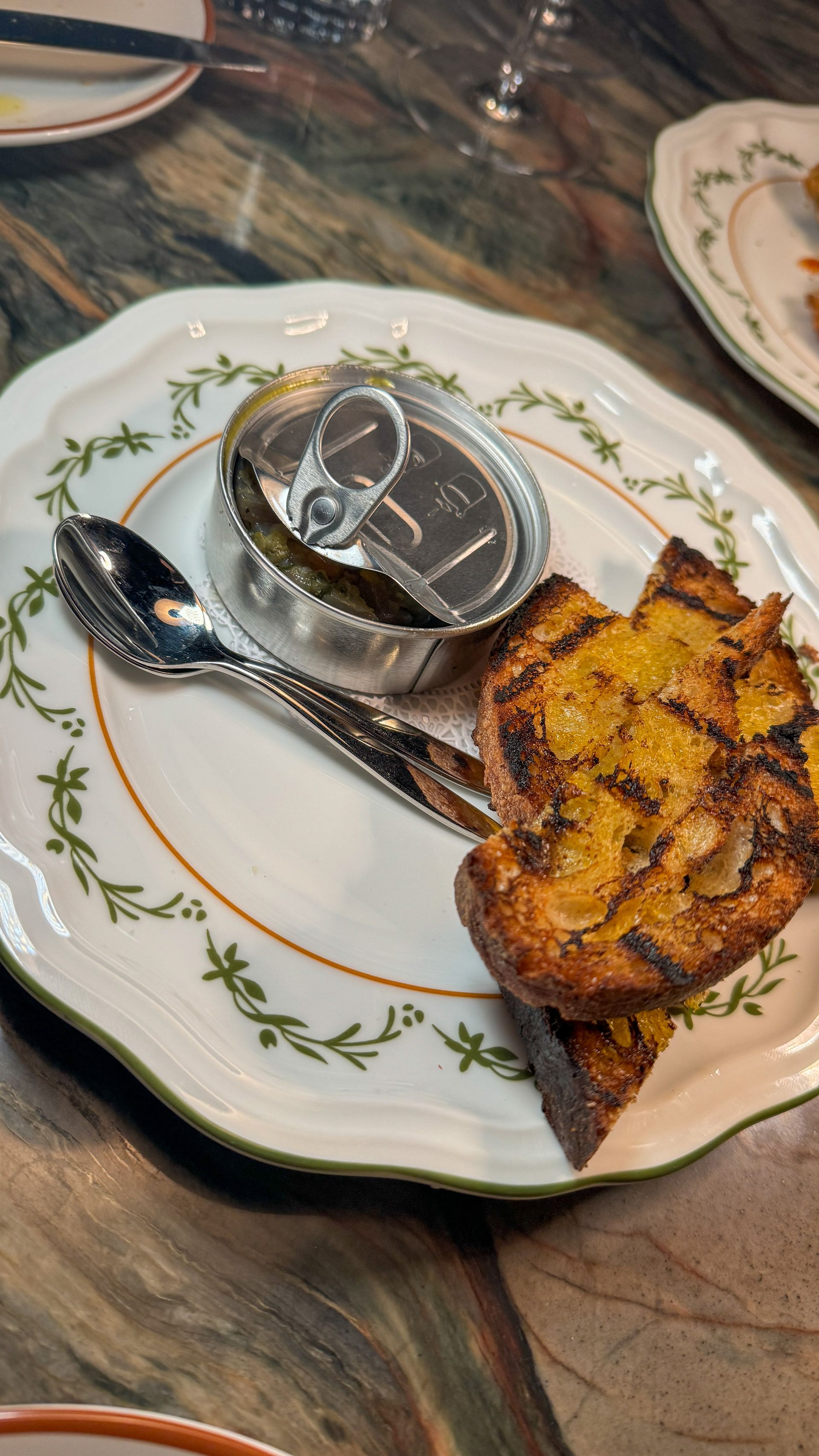 A plate of food with a can of sardines and a spoon on a table.