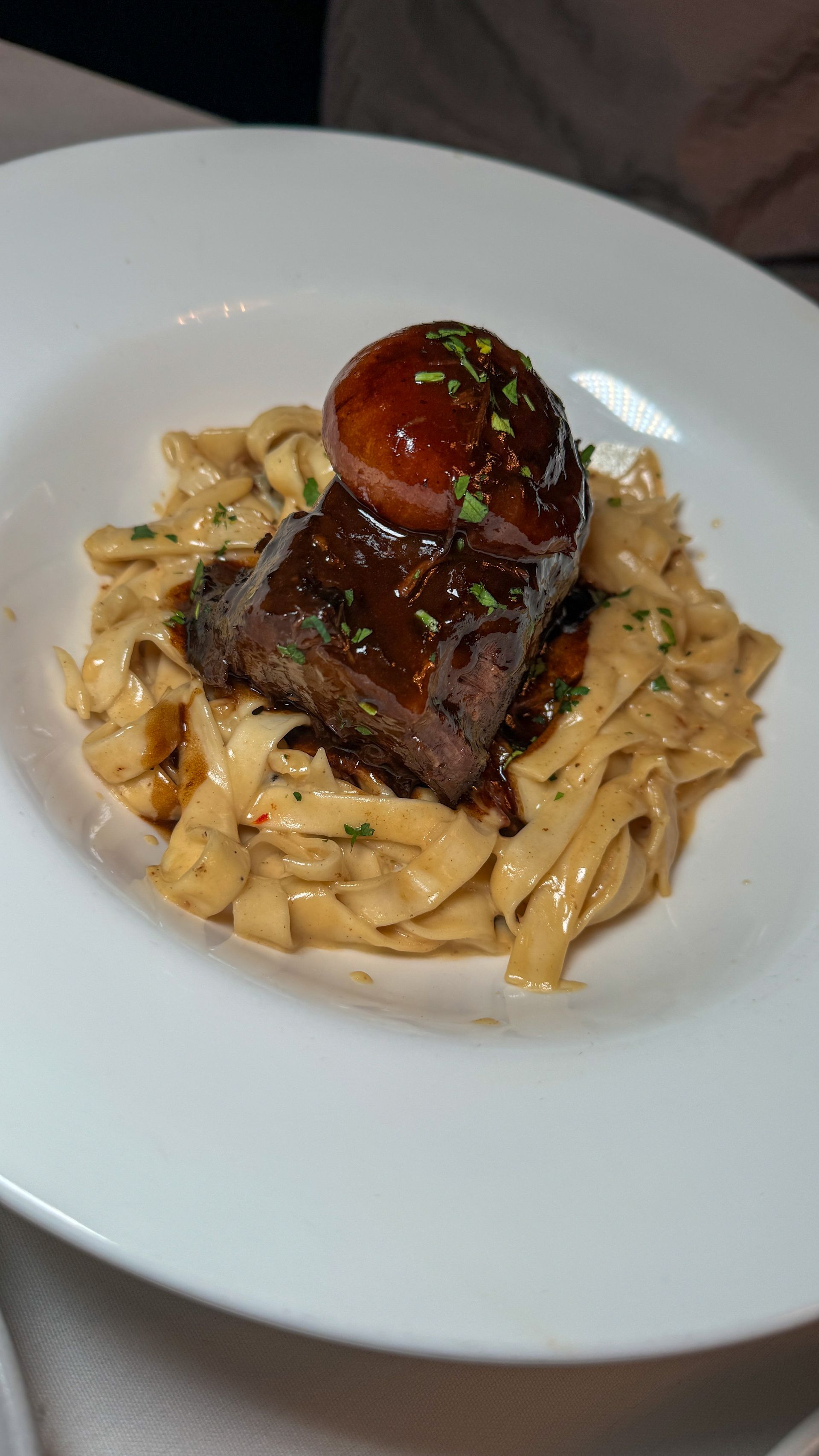 A white plate topped with noodles and meat on a table.