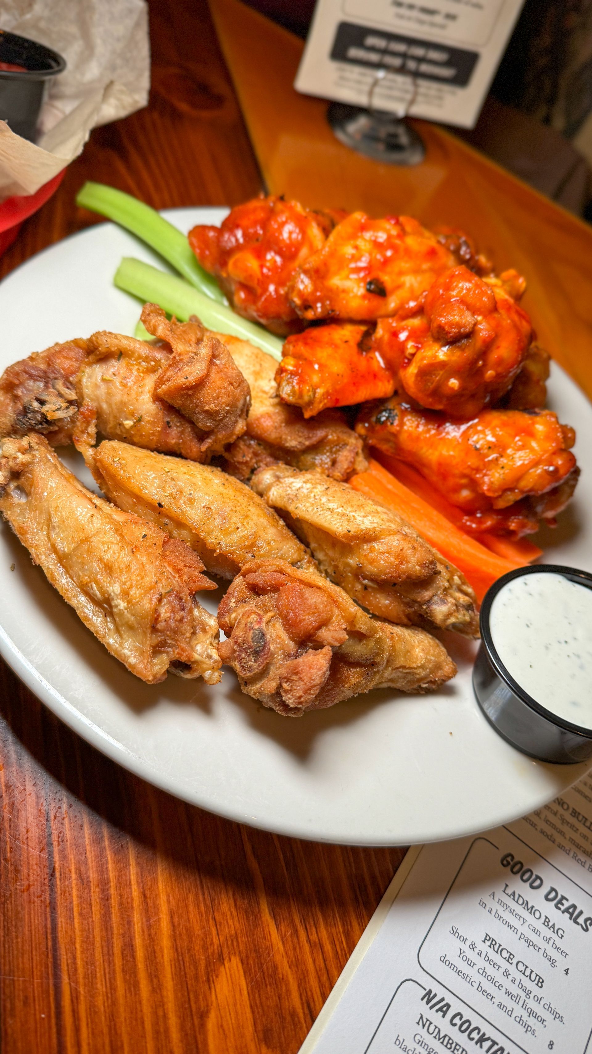 A plate of chicken wings with celery and carrots on a wooden table.