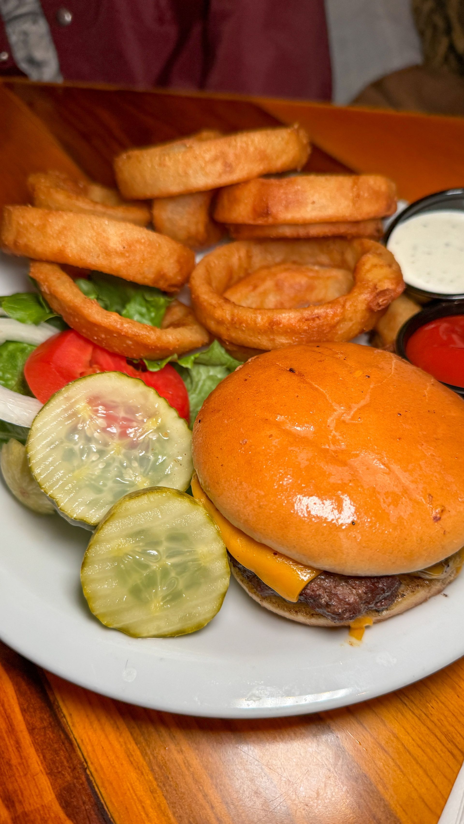 A hamburger and onion rings on a white plate on a wooden table.