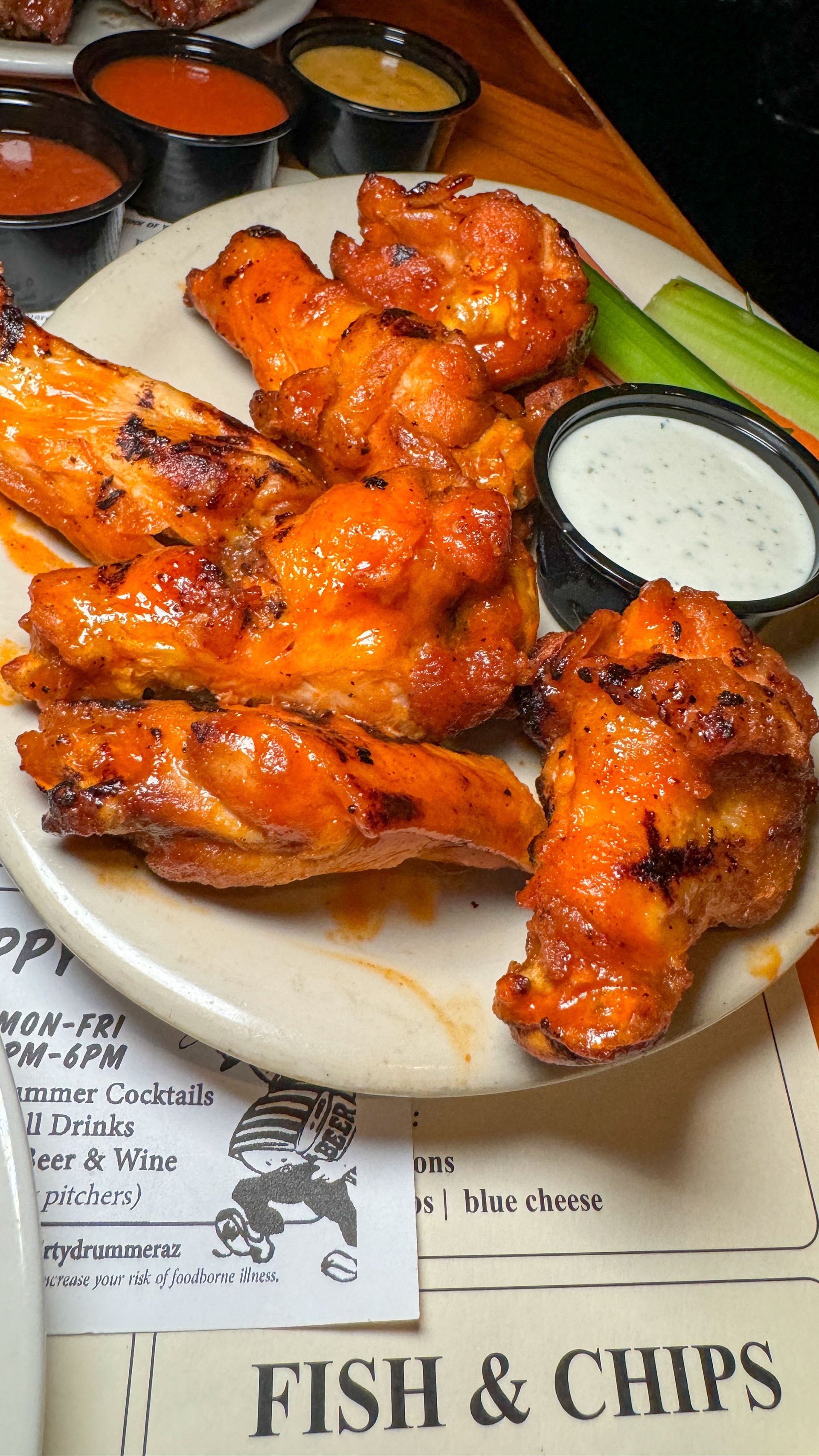 A plate of chicken wings with ranch dressing and celery sticks on a table.