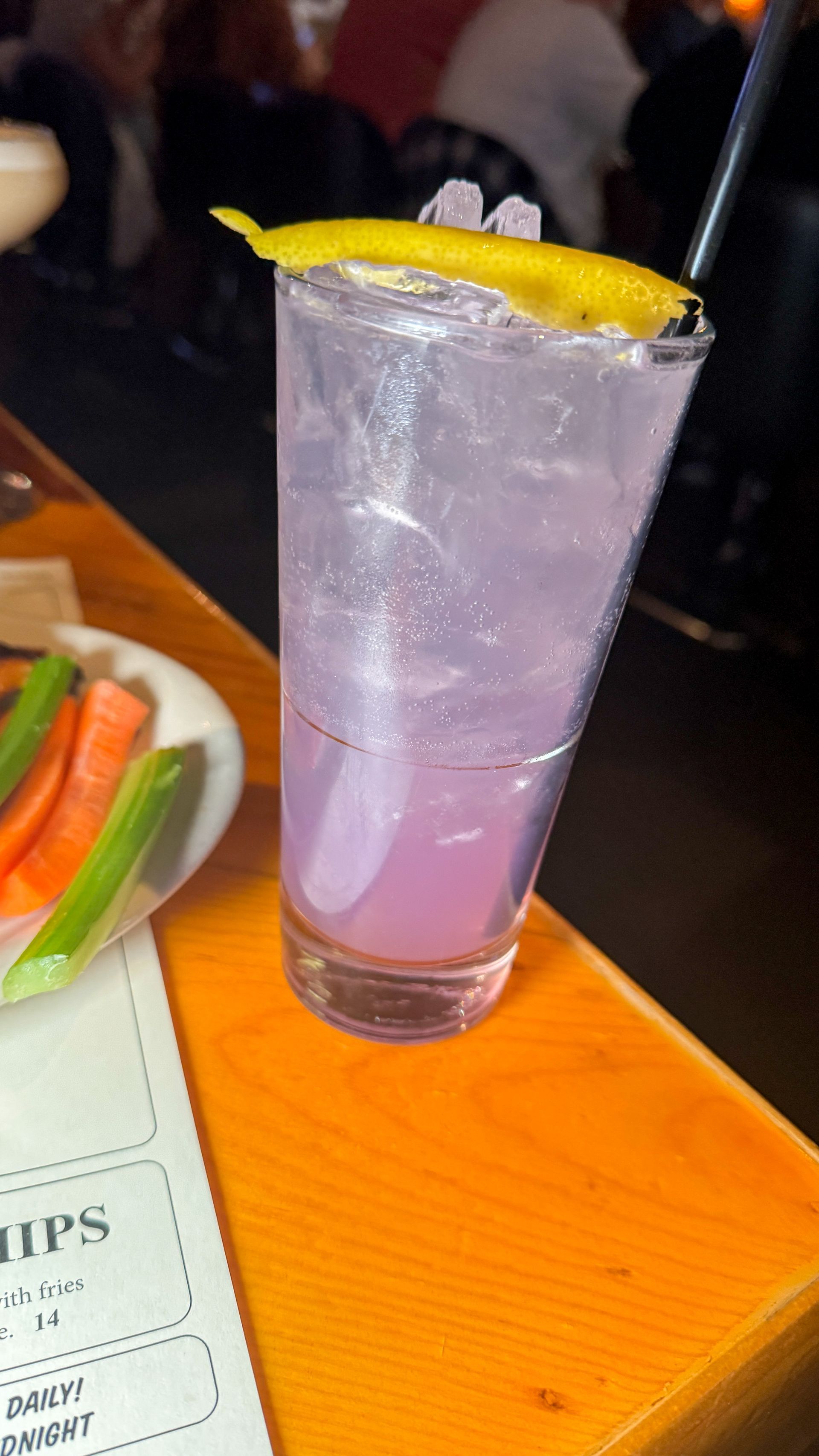 A tall glass of purple liquid with a straw on a table.