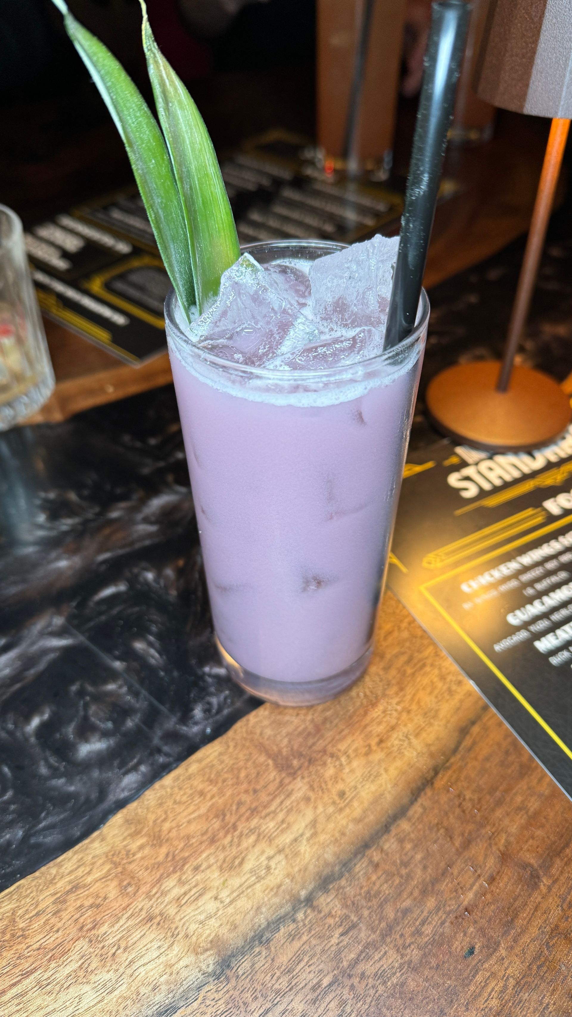 A purple drink in a tall glass with a straw on a wooden table.