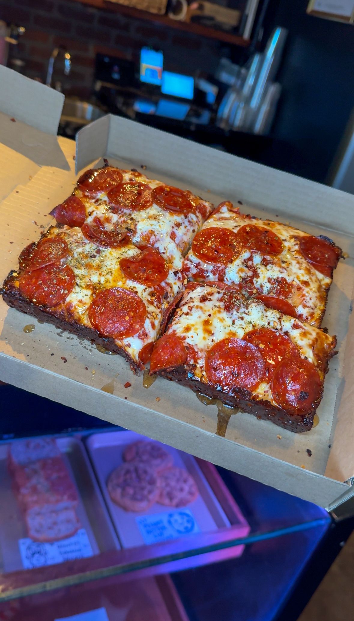 Square pepperoni pizza in a cardboard box, with melted cheese and crispy edges.