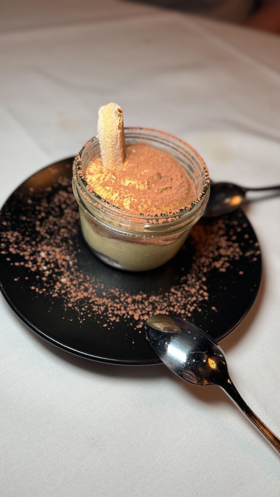 A dessert in a jar on a black plate with a spoon.
